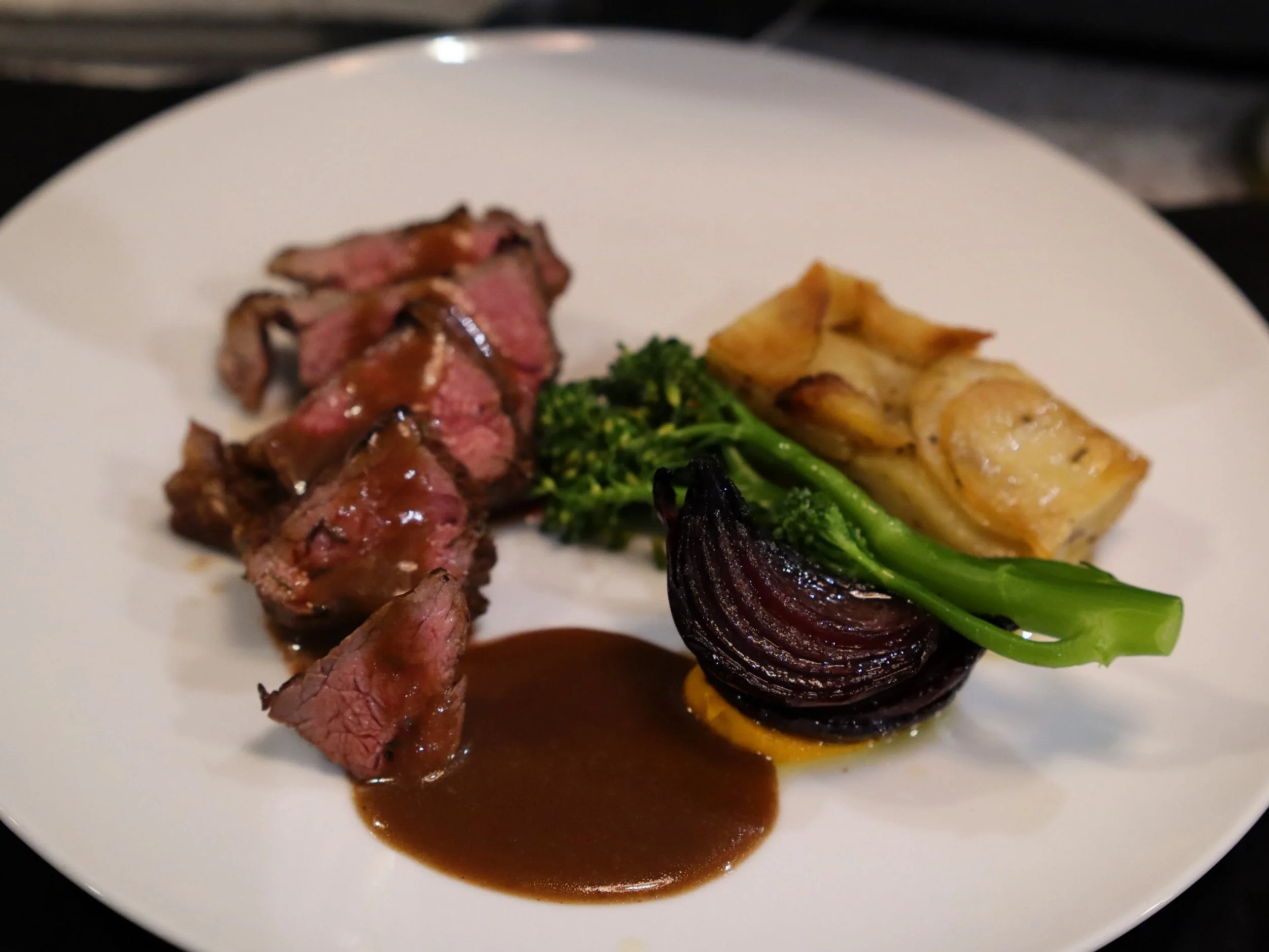 Sliced roast meat with jus, broccolini, roasted onion and layered potato gratin.
