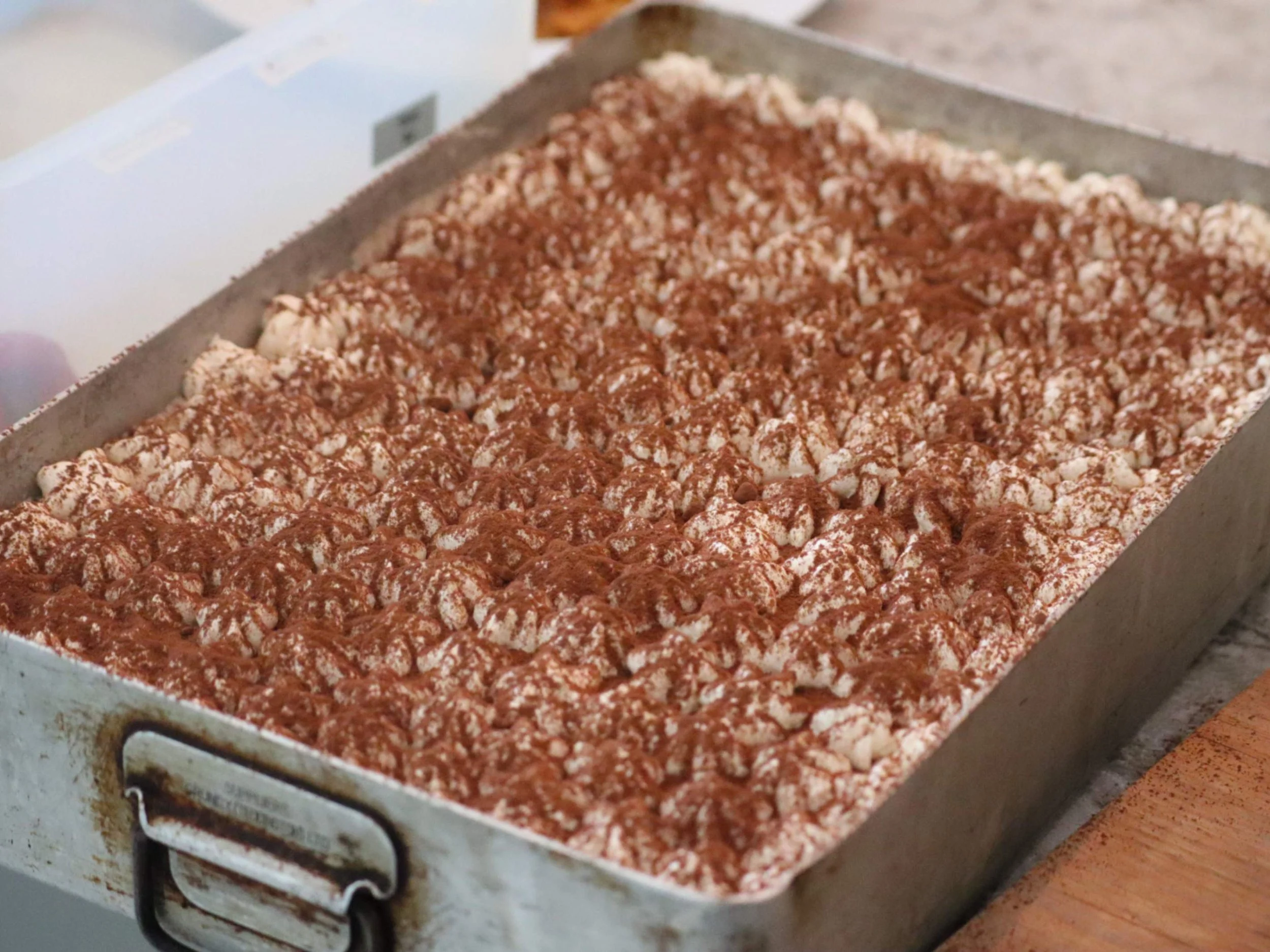 Large tray of homemade tiramisu dusted with cocoa for event catering.