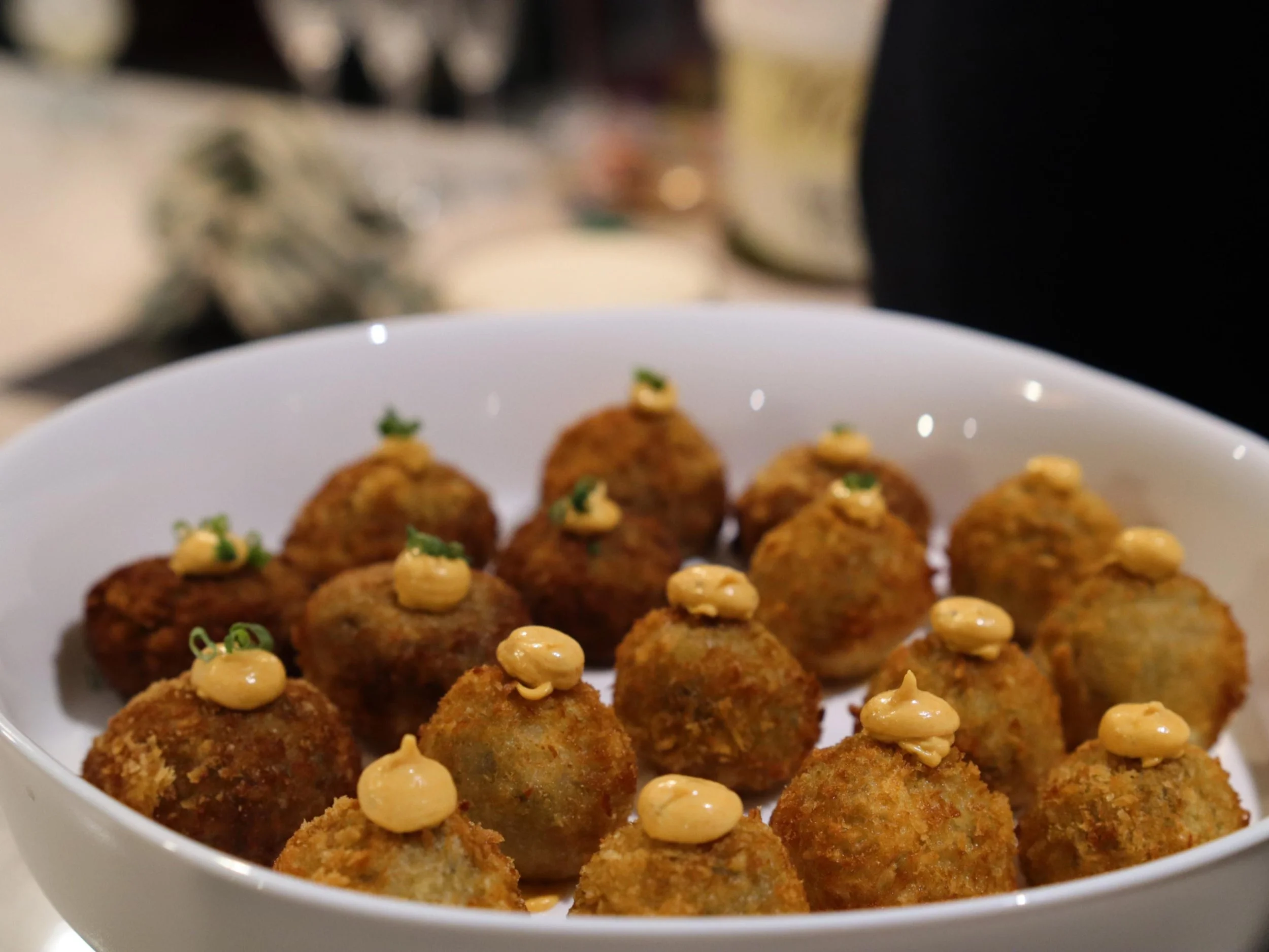  Golden savoury croquettes topped with spiced sauce and herbs in a serving bowl.
