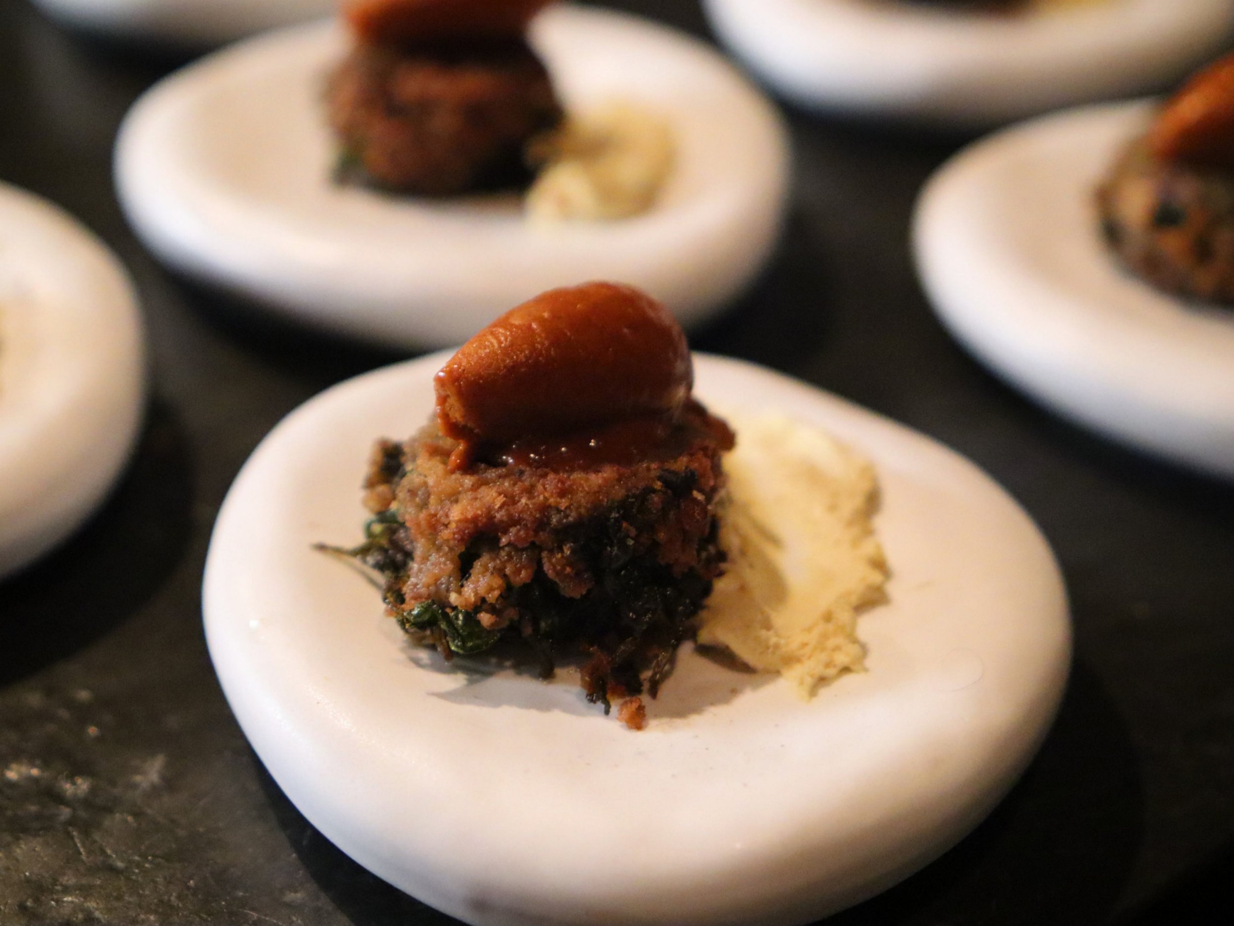 Small plated savoury canapé with a crisp topping, dark greens and spiced sauce.
