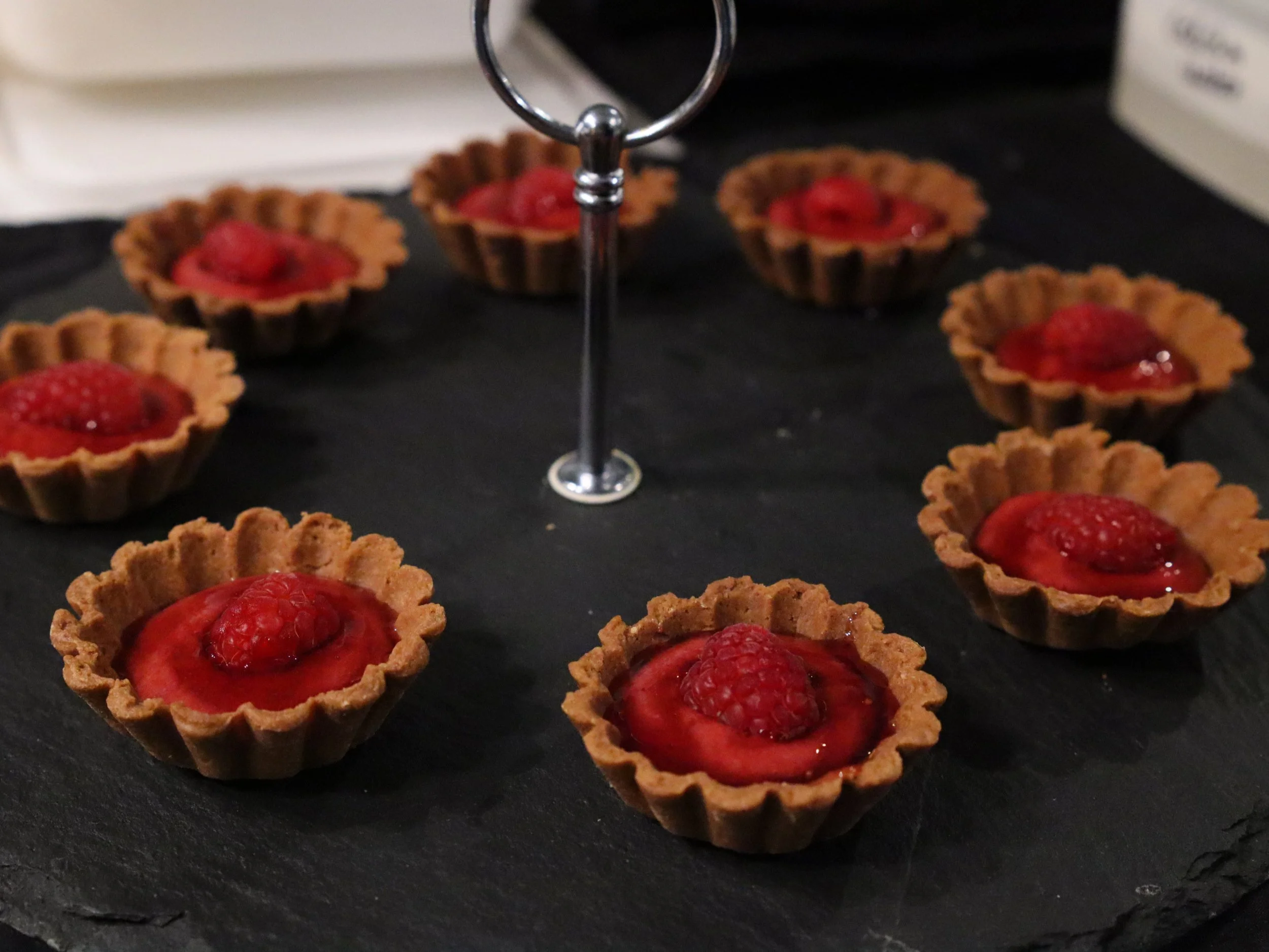 Mini raspberry tartlets arranged on a slate serving stand for dessert service.
