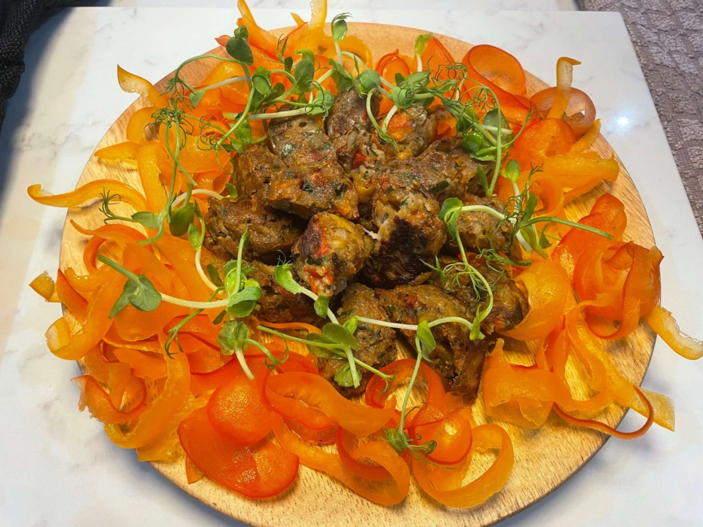 Jamaican-style spiced meat pieces arranged with bright orange vegetable ribbons and pea shoots.
