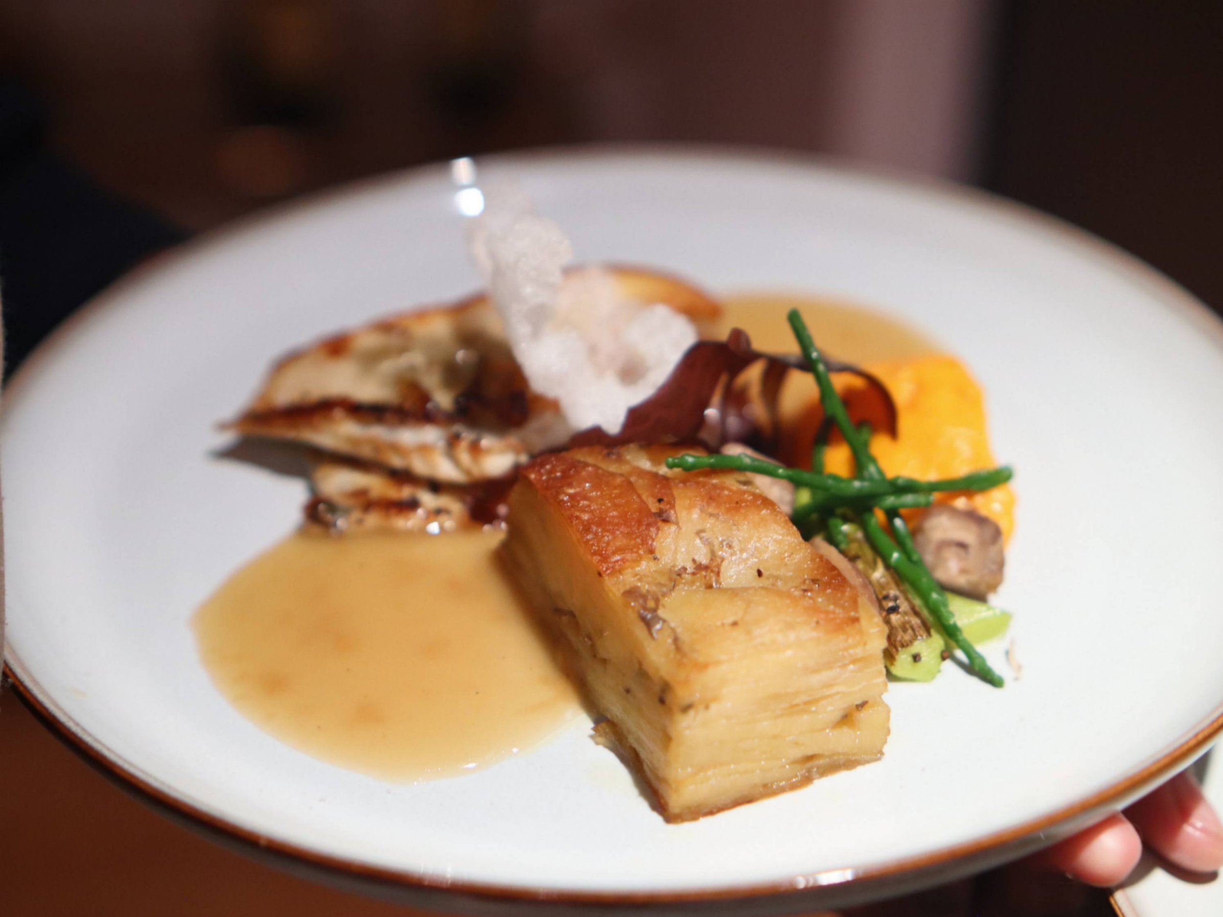 Fine dining main course with layered potato terrine, grilled vegetables and rich sauce.