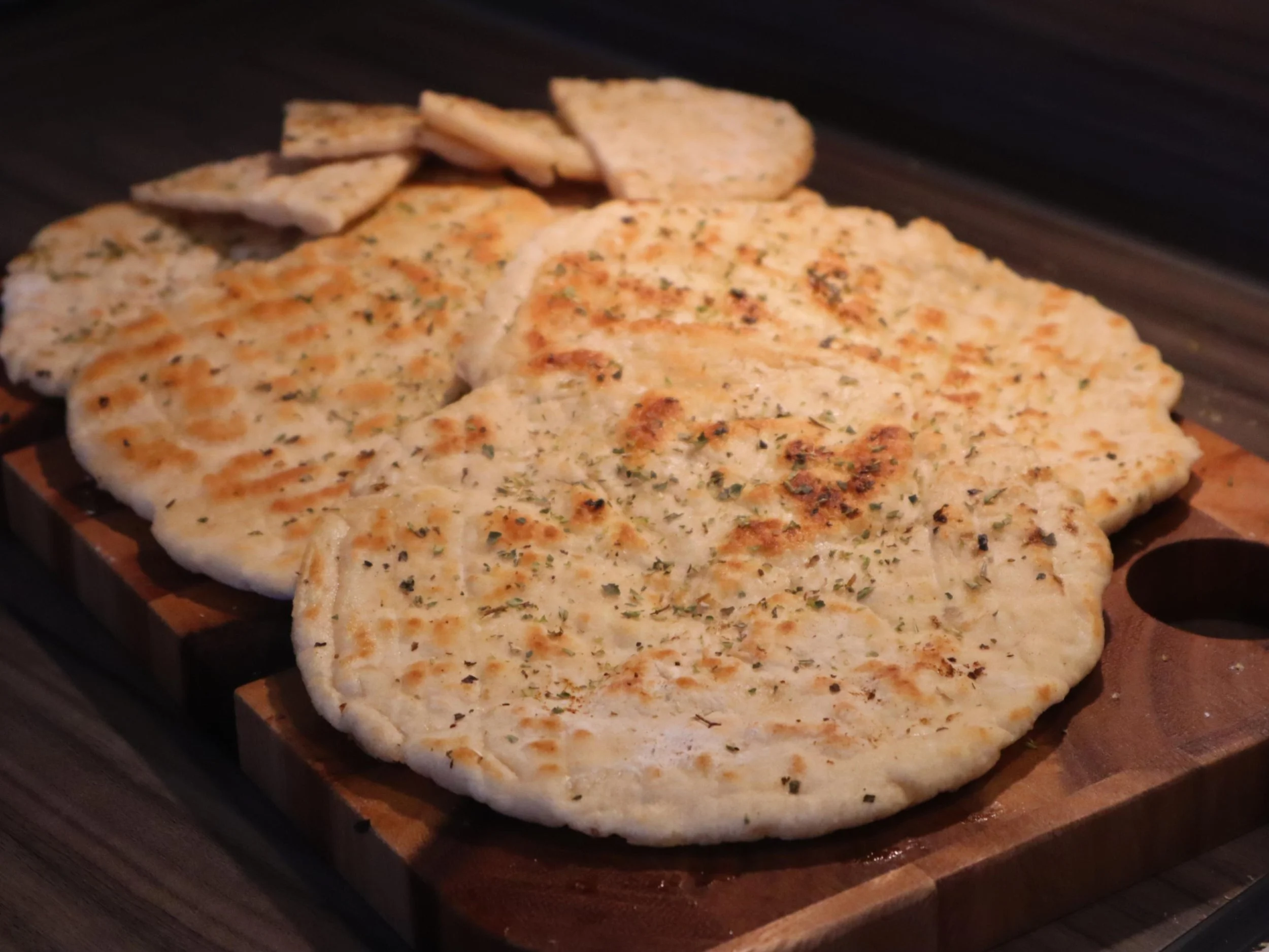 Freshly cooked Greek pita breads brushed with olive oil and herbs on a wooden board.
