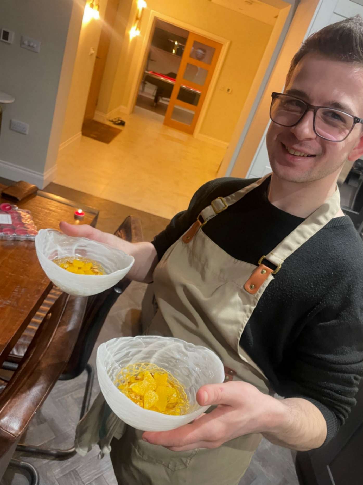 Greek Tings chef holding two orange plated dessert courses during private dining service.

