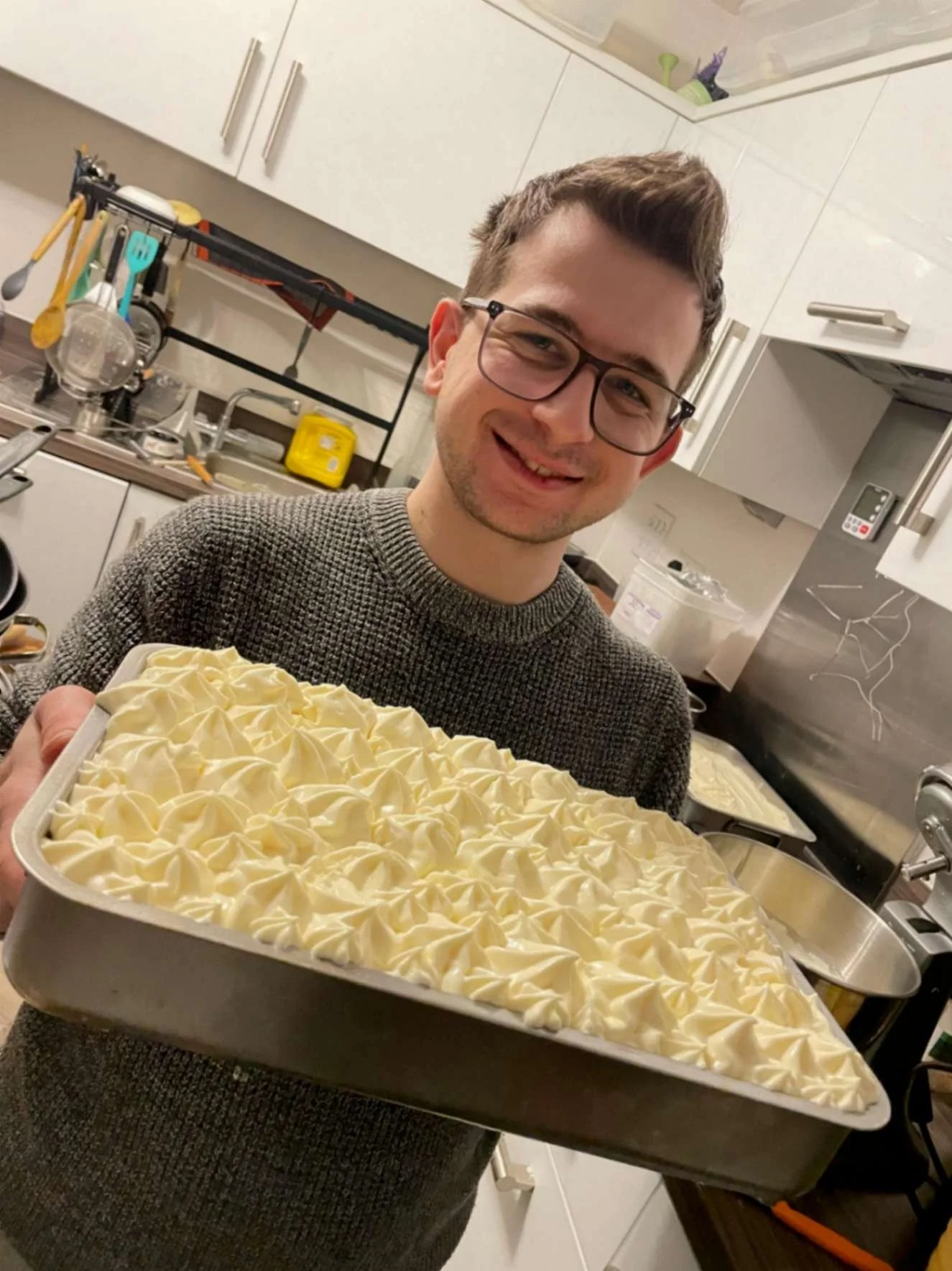 Greek Tings chef holding a freshly prepared tray of piped tiramisu cream.
