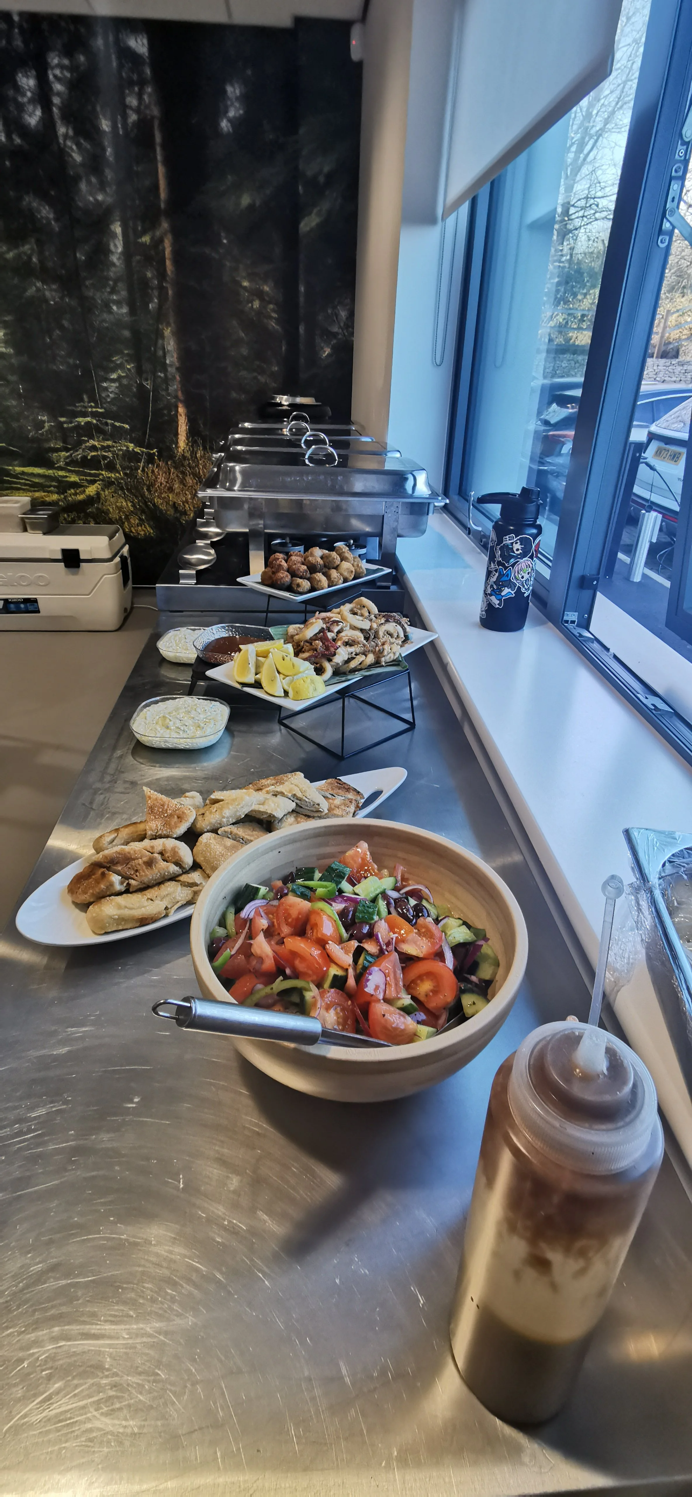 Greek-style catering buffet with salad, pita, dips and hot dishes ready for guests.
