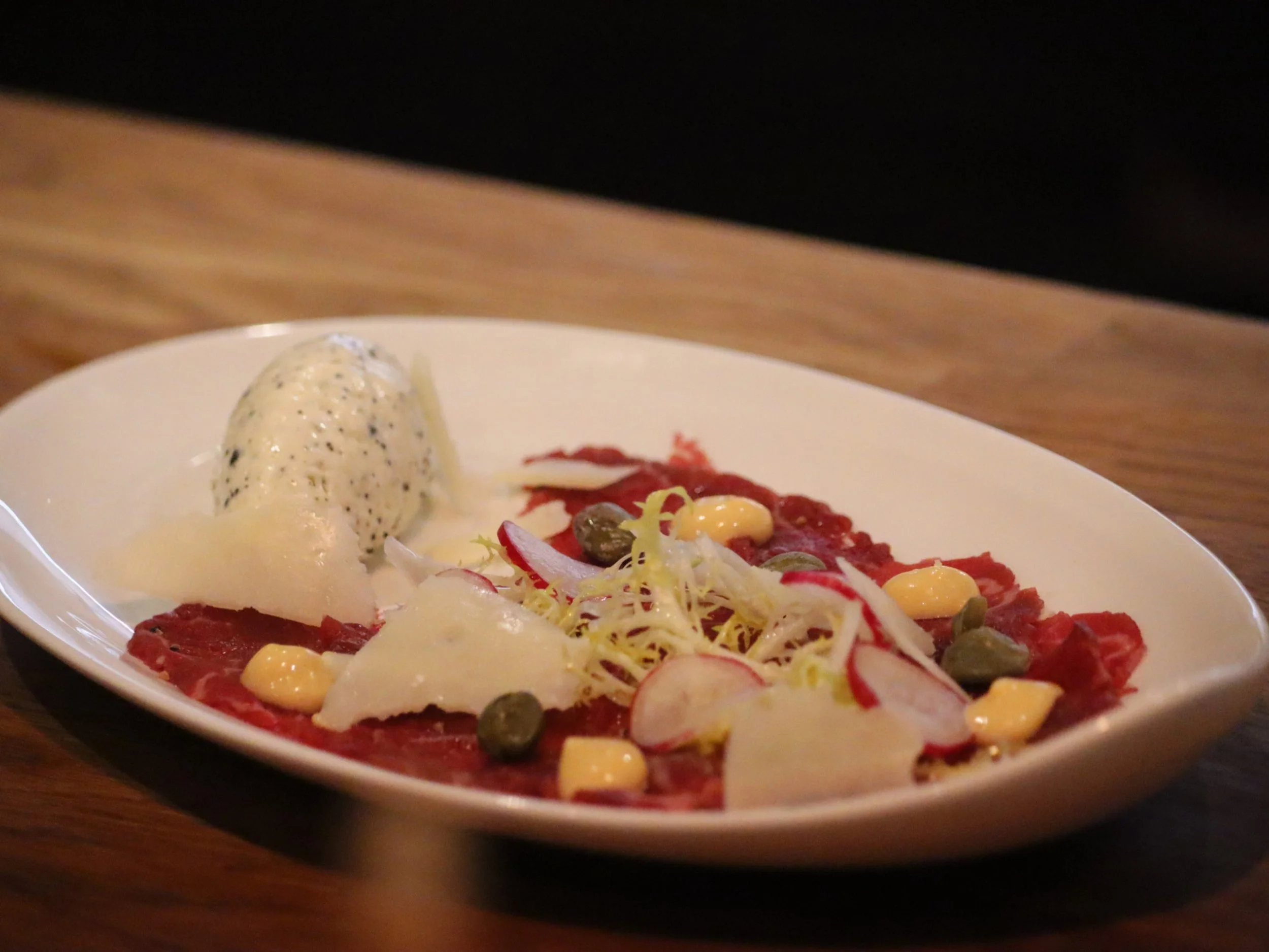 Beef carpaccio with radish, capers, dressed leaves and a creamy quenelle.
