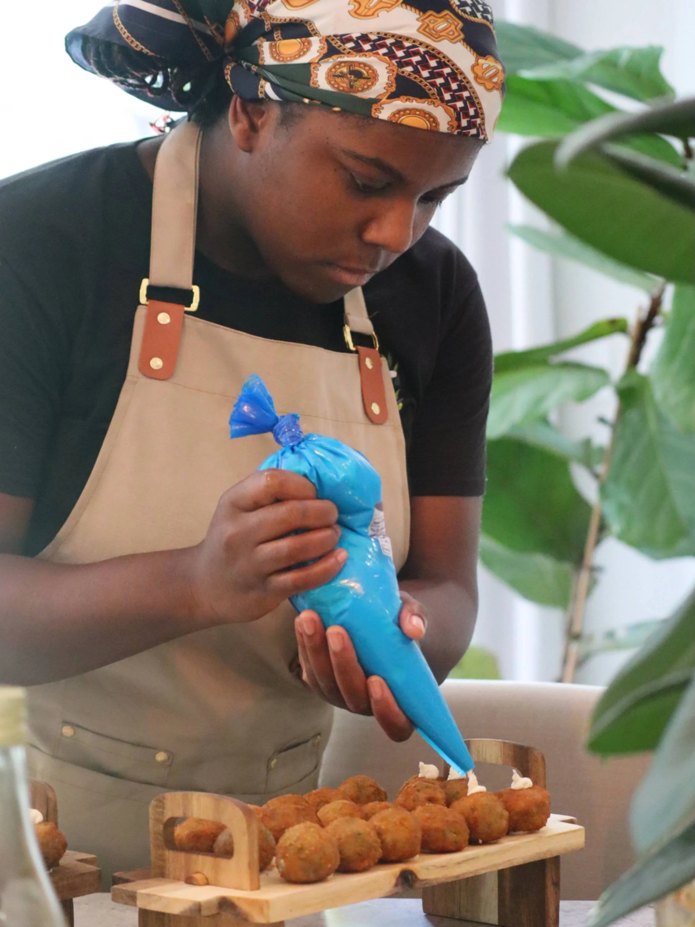 Greek Tings chef piping sauce onto golden croquettes during event preparation.
