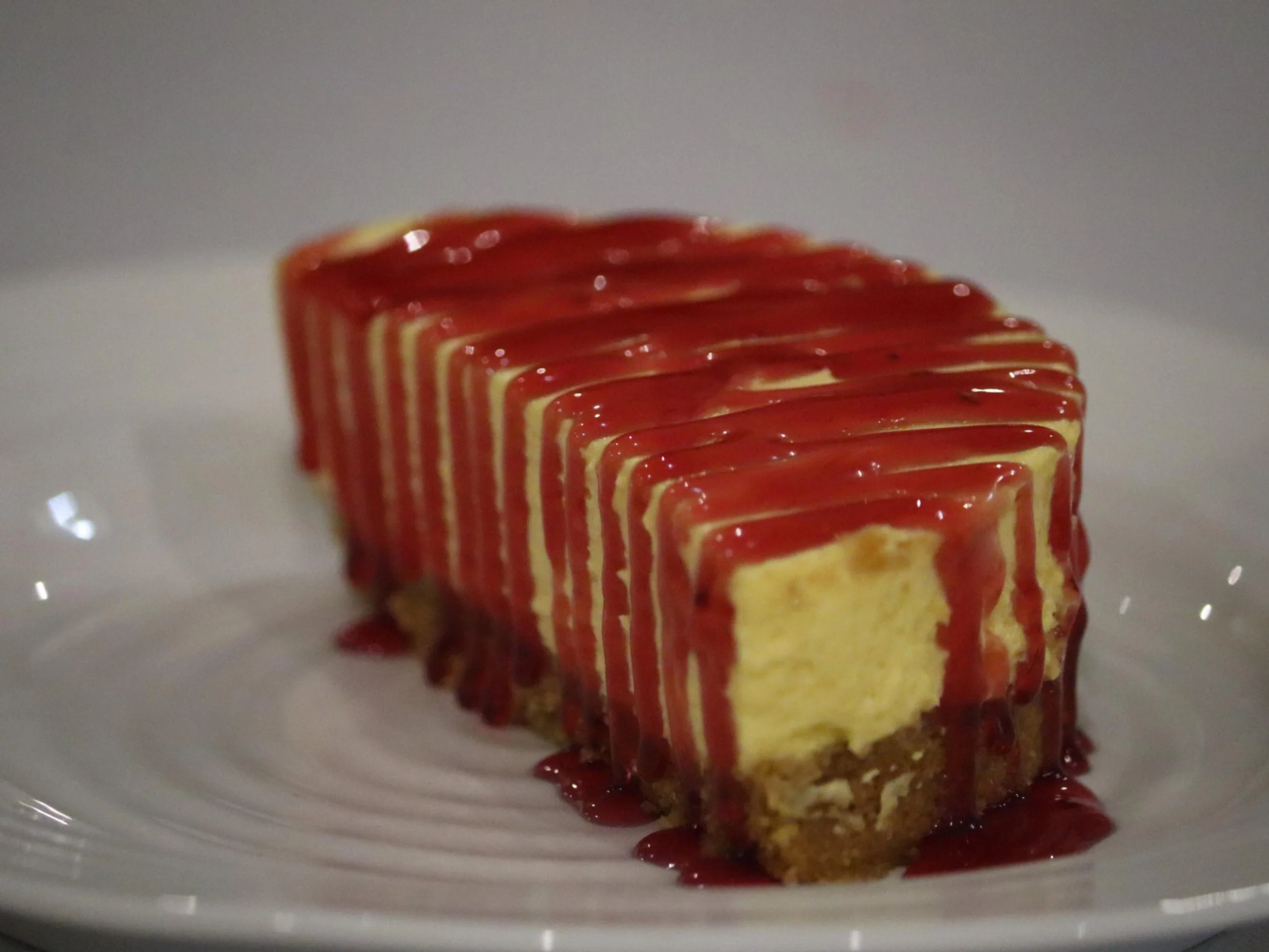 Cheesecake portion finished with raspberry sauce and biscuit crumb