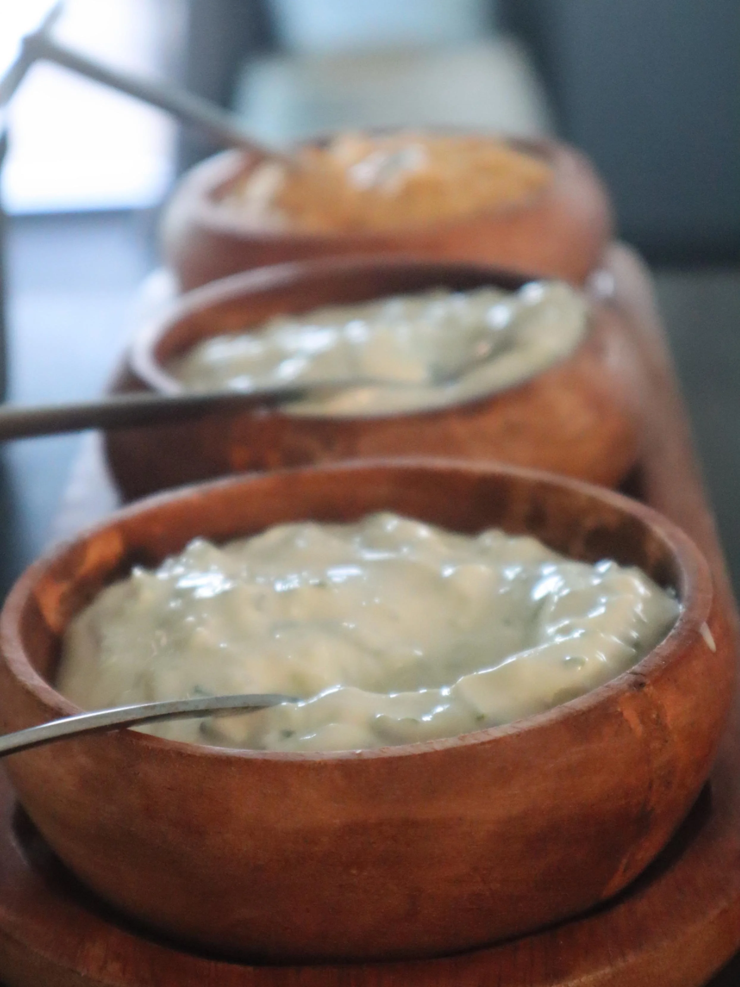 Greek dips served in wooden bowls, including creamy tzatziki and other house-made condiments.