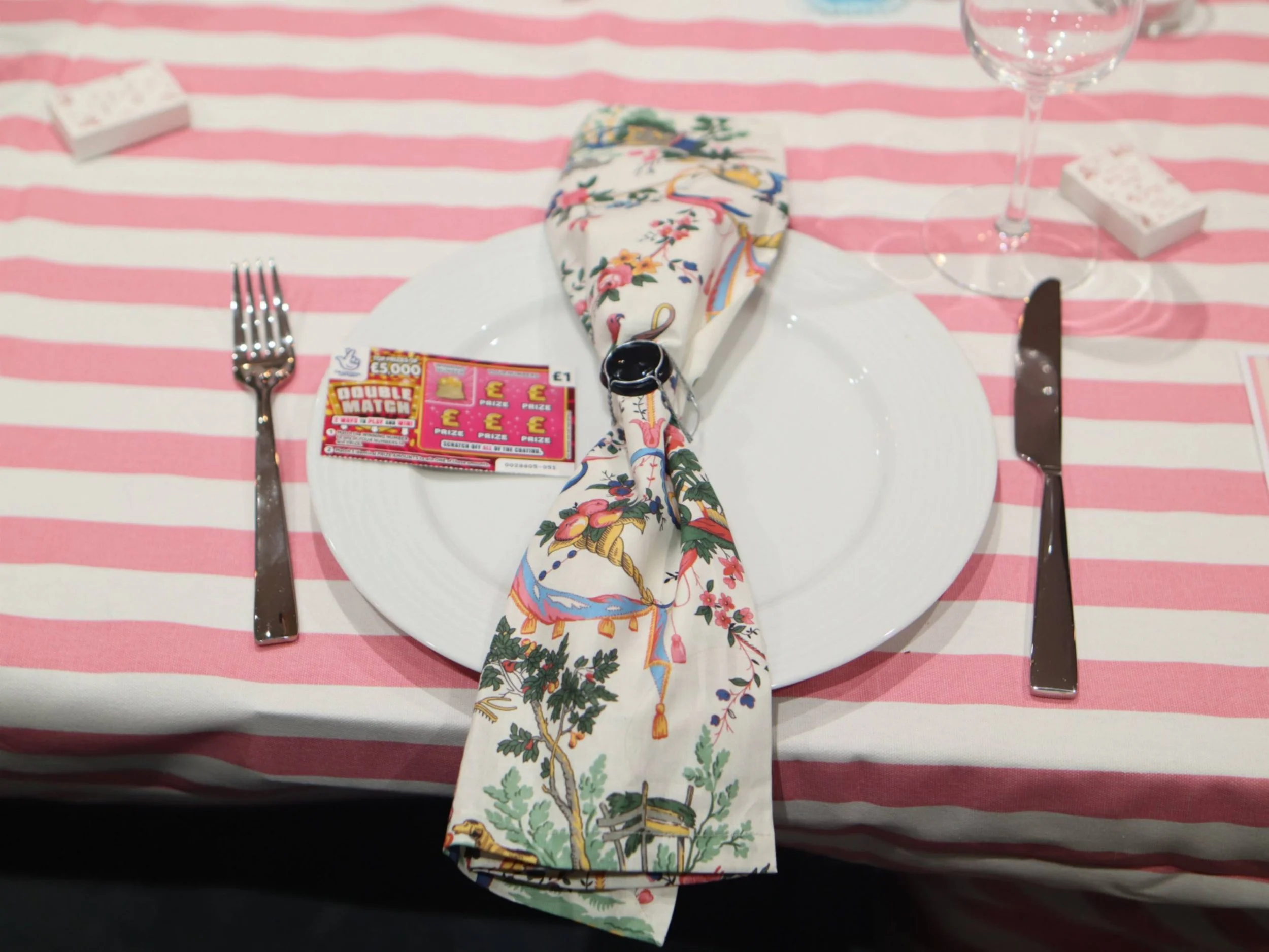 Pink striped themed table setting with floral napkin, white plate and playful table favour.
