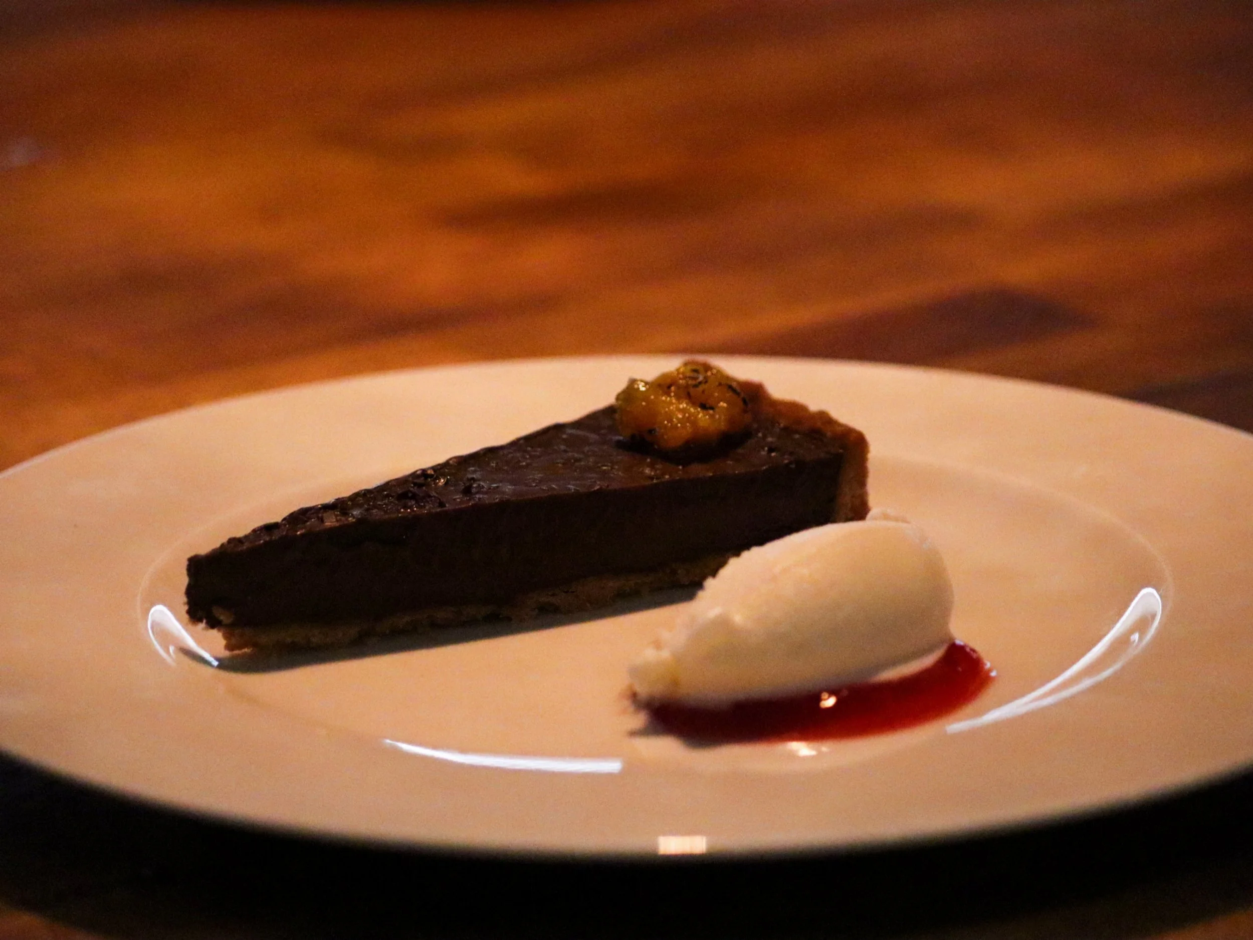 Chocolate tart slice served with a white quenelle and red fruit sauce.