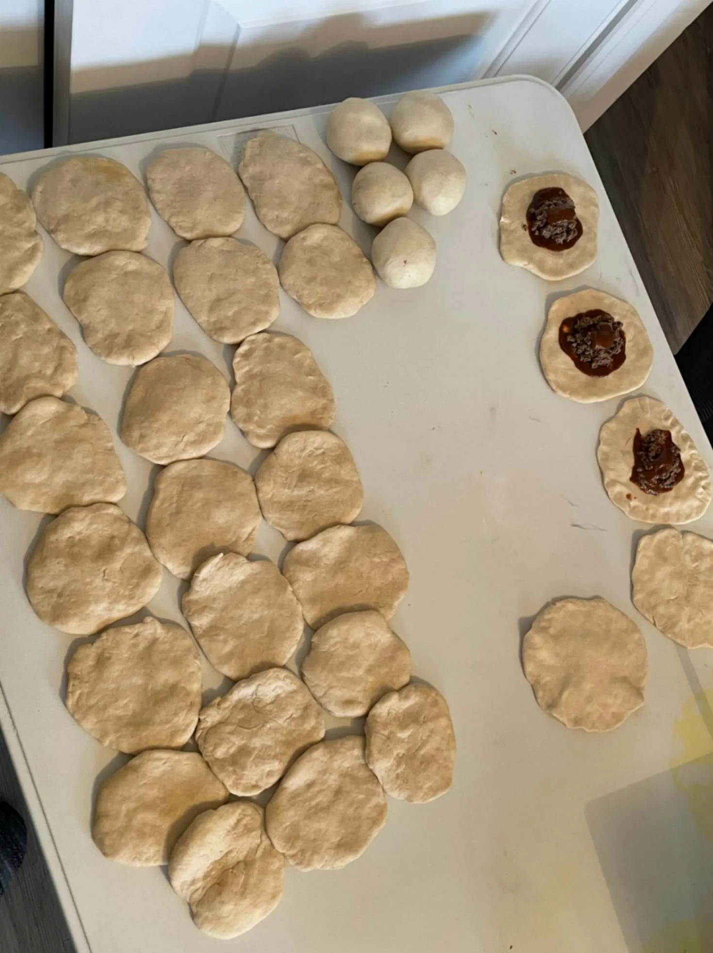 Rounds of handmade dough being shaped and filled during Greek Tings kitchen preparation.
