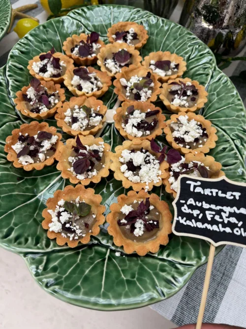 Mini aubergine and feta tartlets with Kalamata olive and micro herbs on a green serving platter