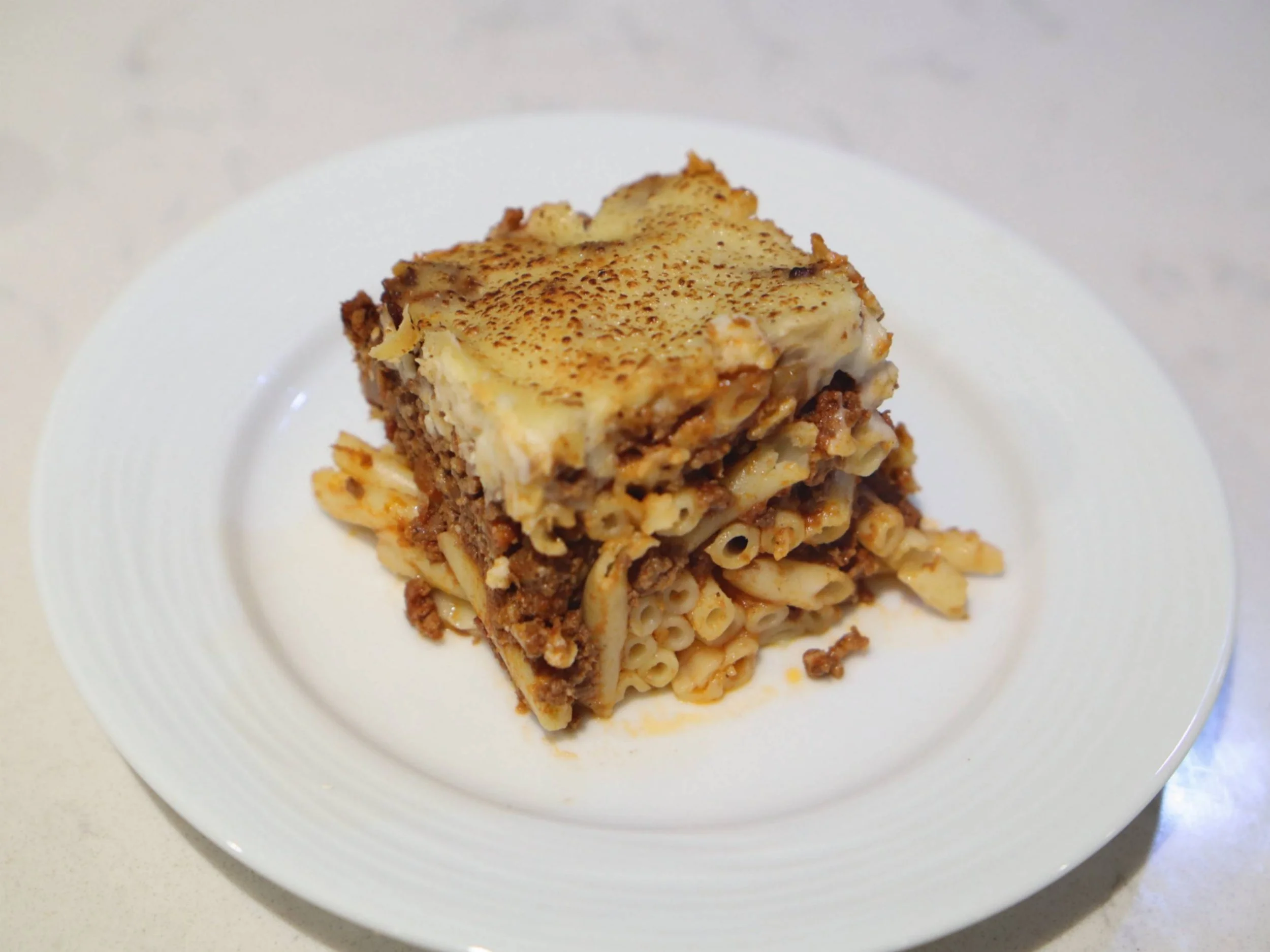 Individual slice of baked pasta (Patitsio) with minced meat and a golden creamy topping.