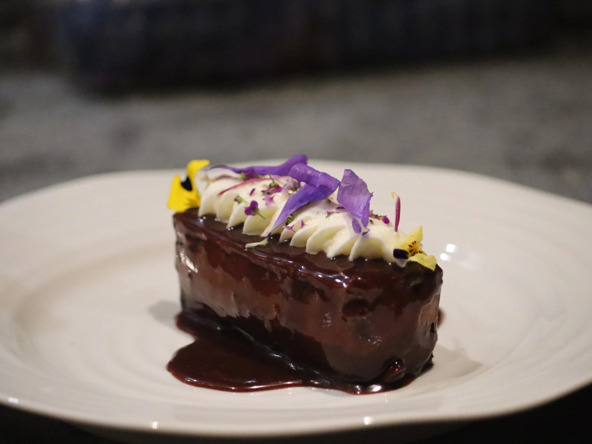 Glossy chocolate dessert topped with piped cream and edible flowers.