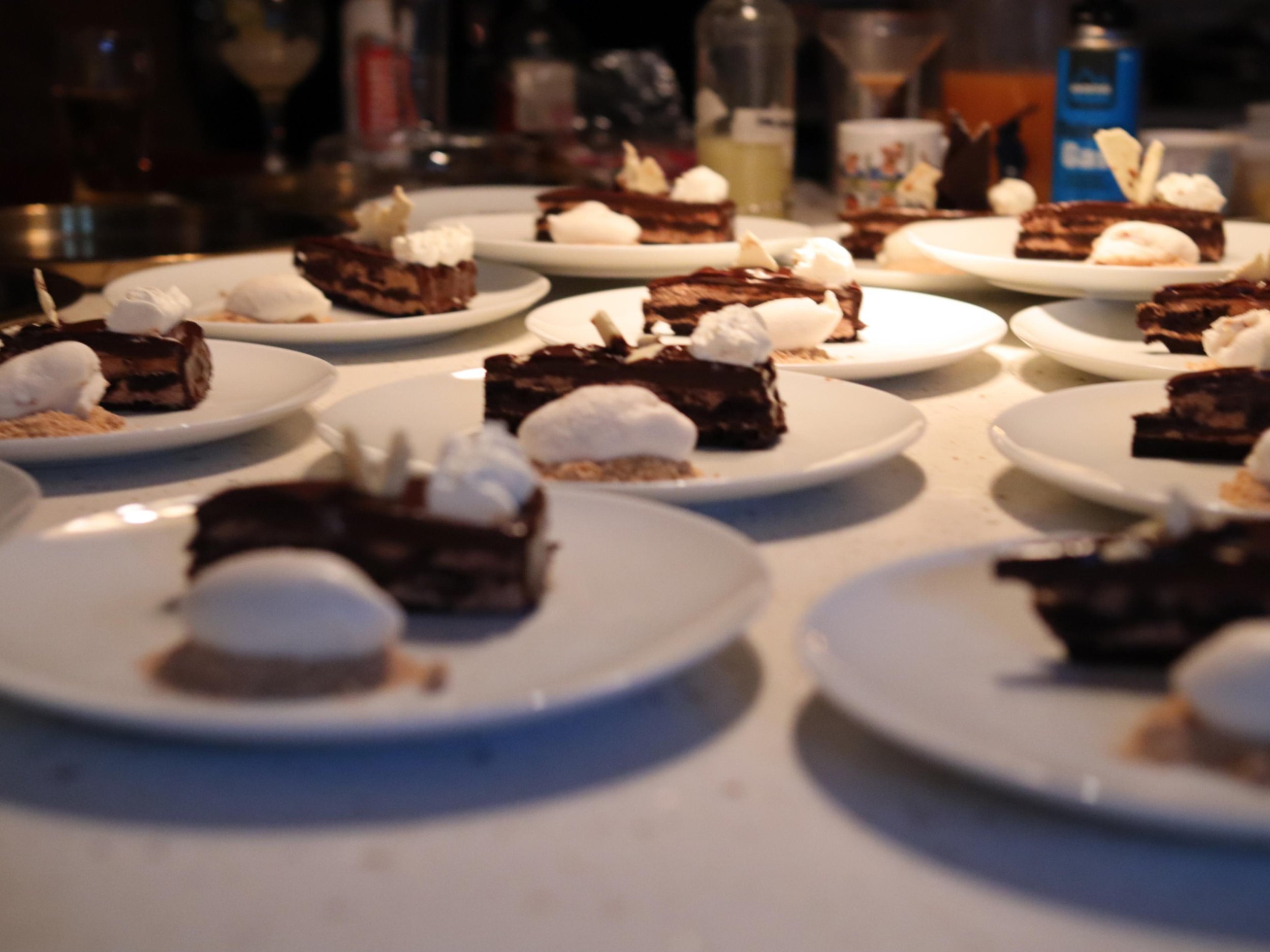Rows of plated chocolate cake desserts with cream and quenelles ready for private dining service.