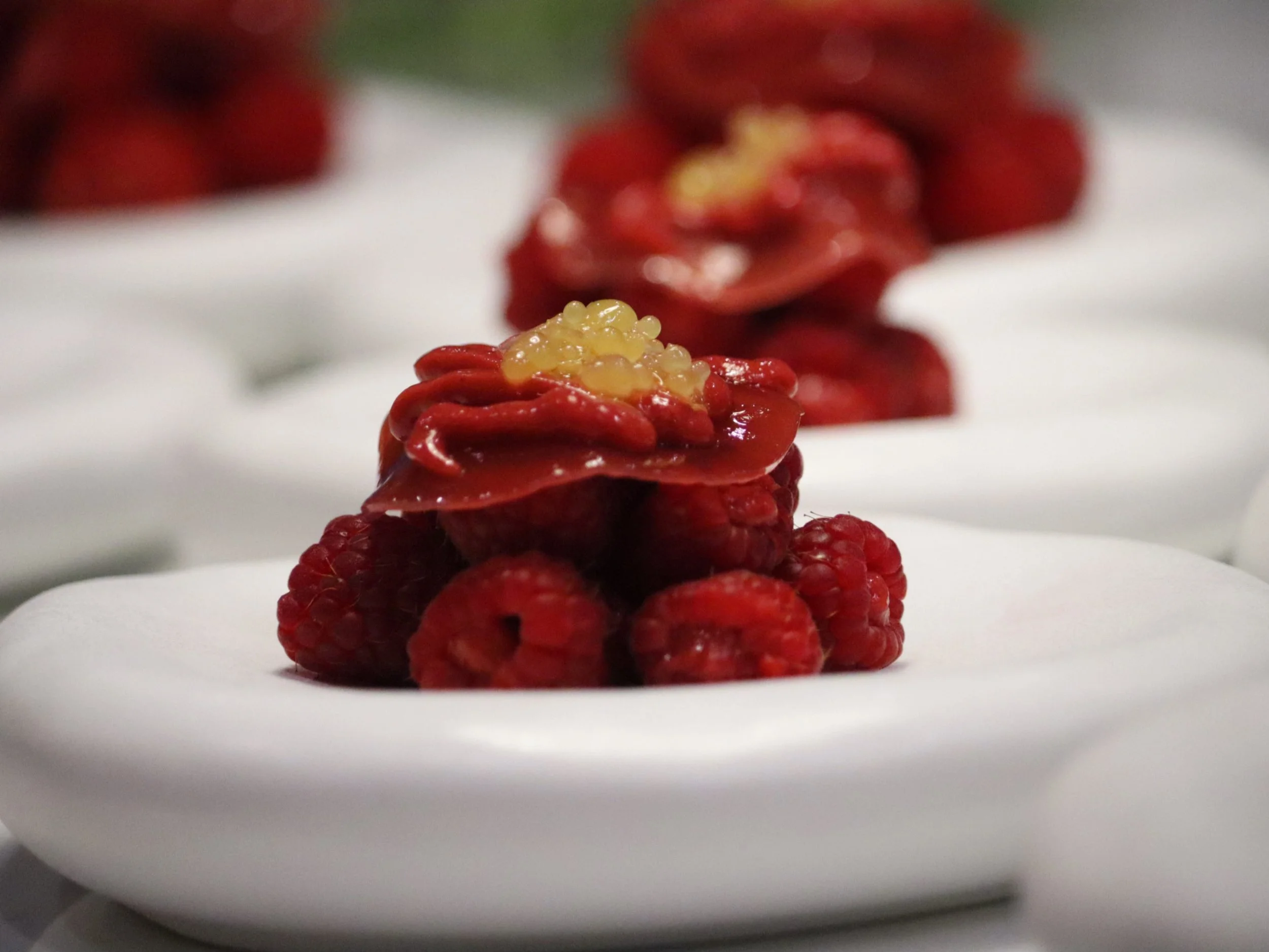 Raspberry dessert with glossy red tuile and citrus pearls on a white plate.