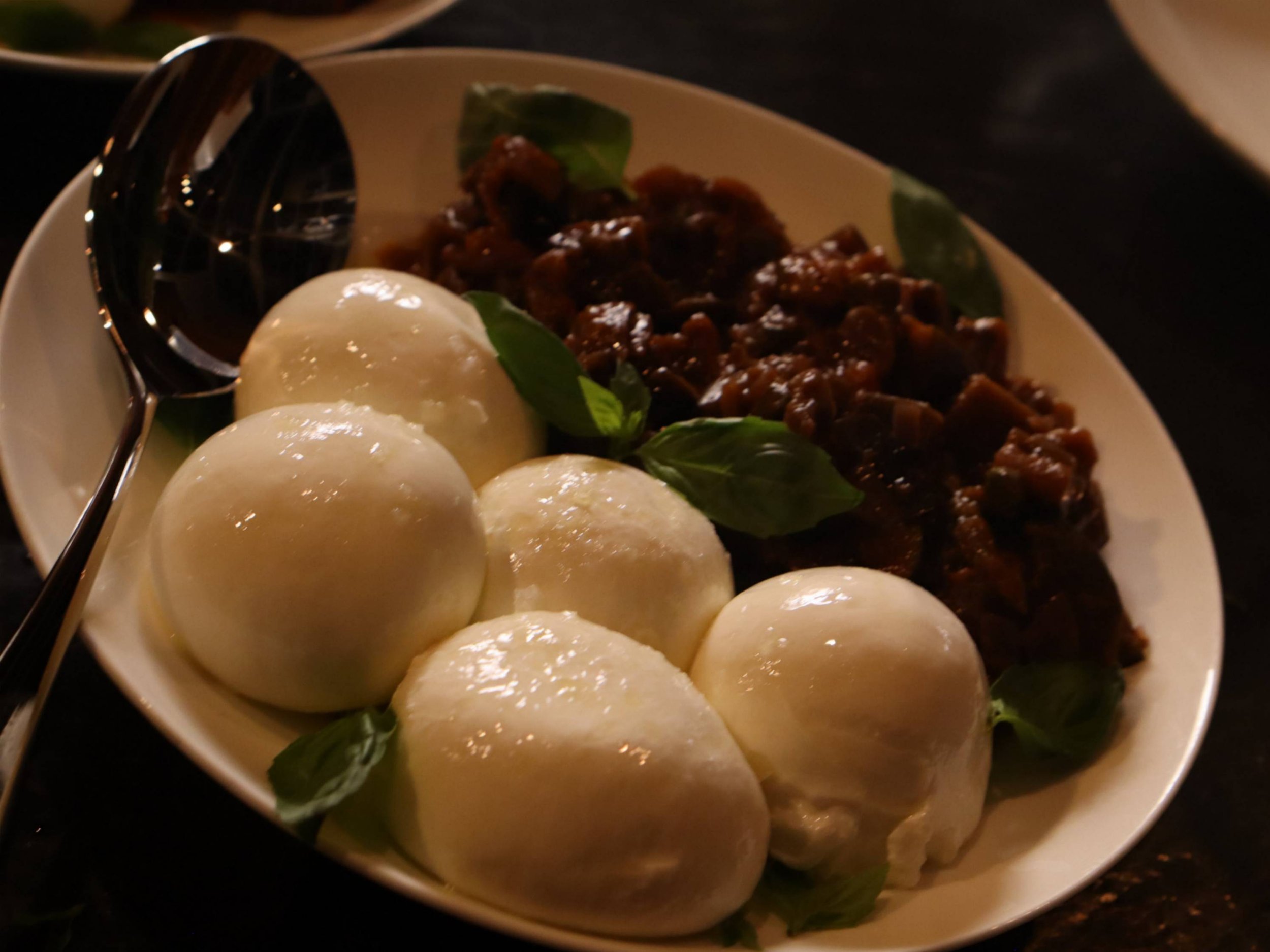 Whole burrata served with aubergine, tomato and fresh basil on an Italian sharing table.