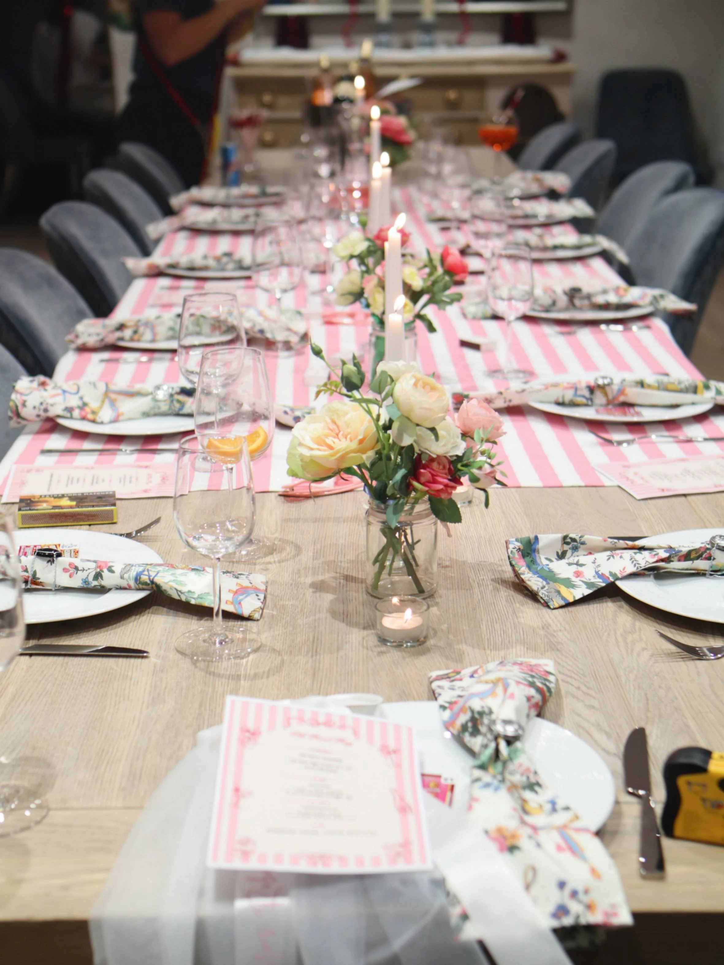 Long pink-and-white themed dinner table with floral napkins, candles and small flower arrangements.