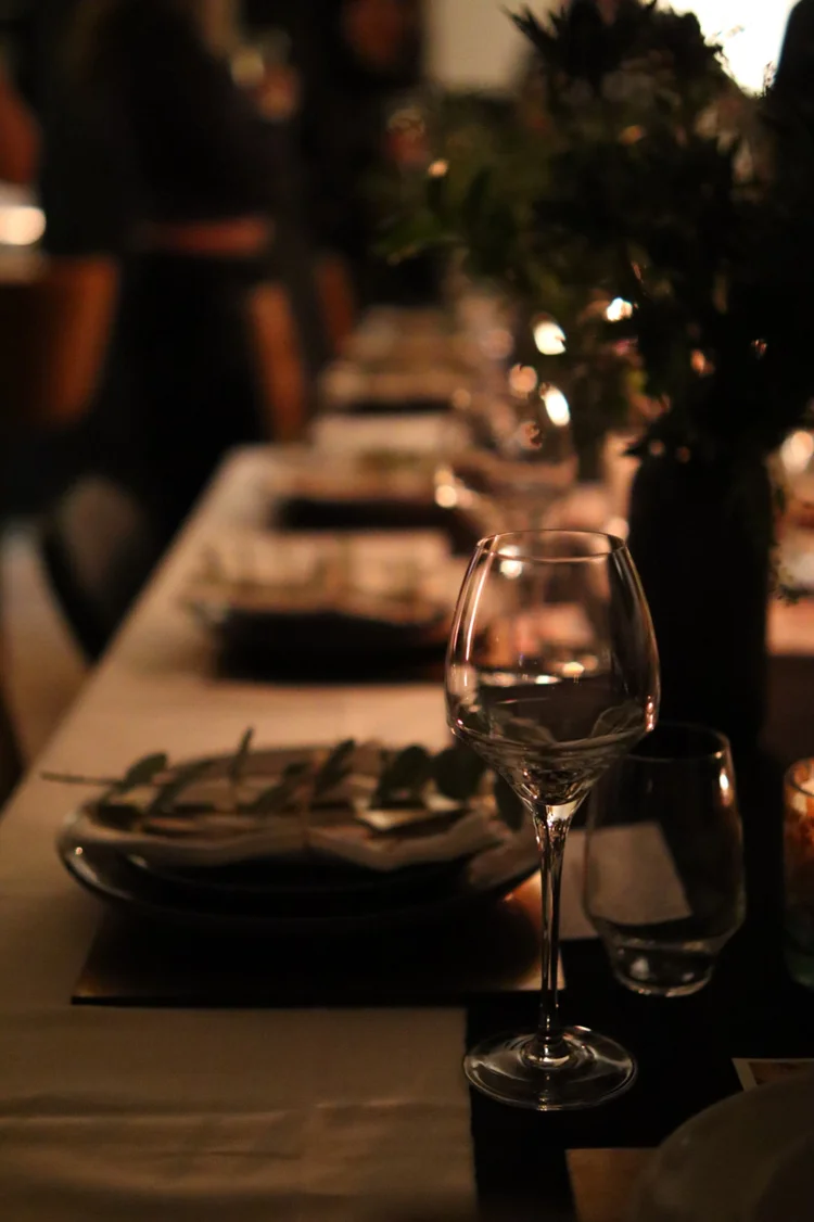 Atmospheric private dining table with wine glass, greenery and elegant place settings at a Greek Tings event.