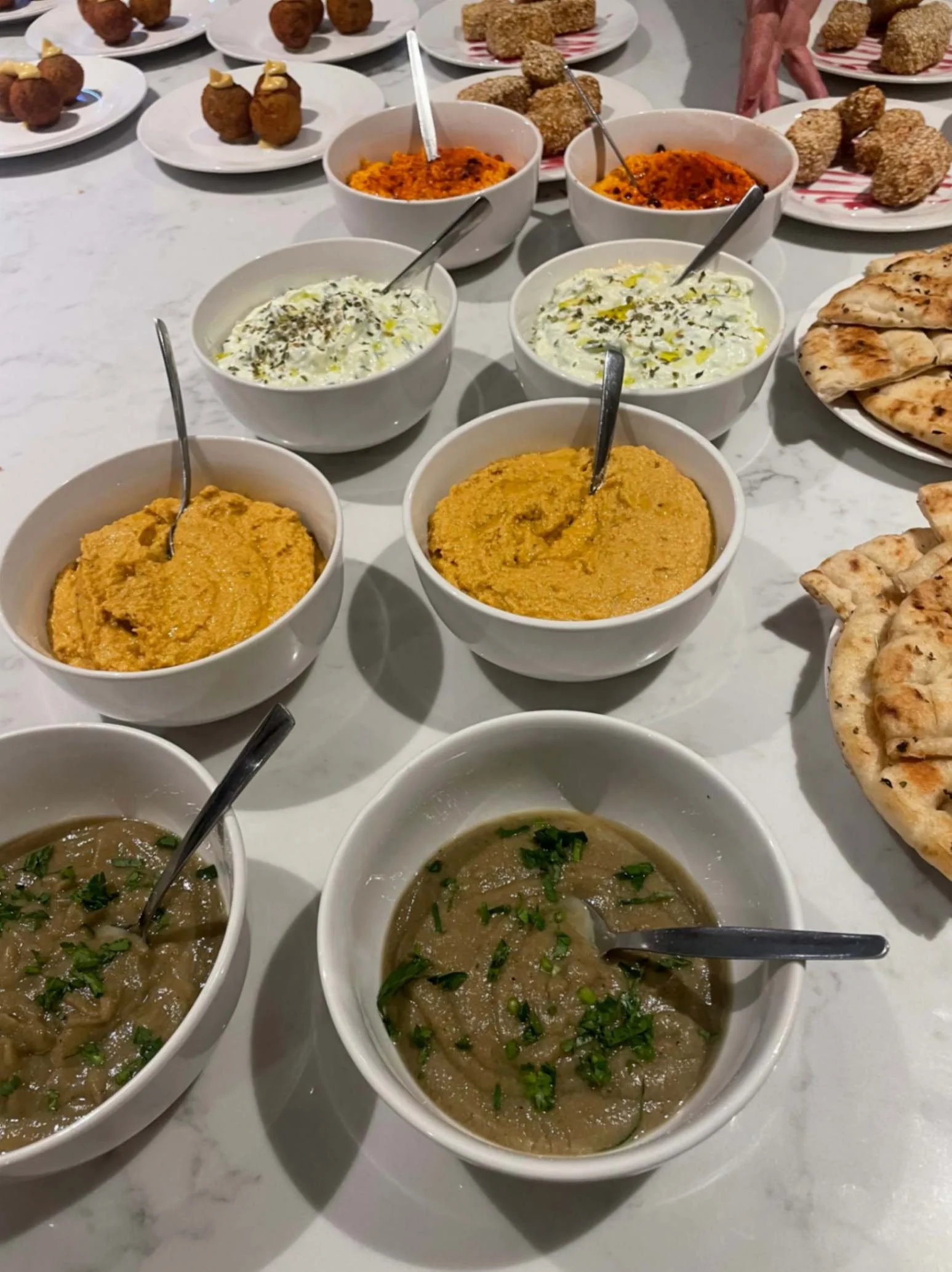Bowls of tzatziki, tirokafteri, aubergine dip and other Greek dips with warm pita bread.
