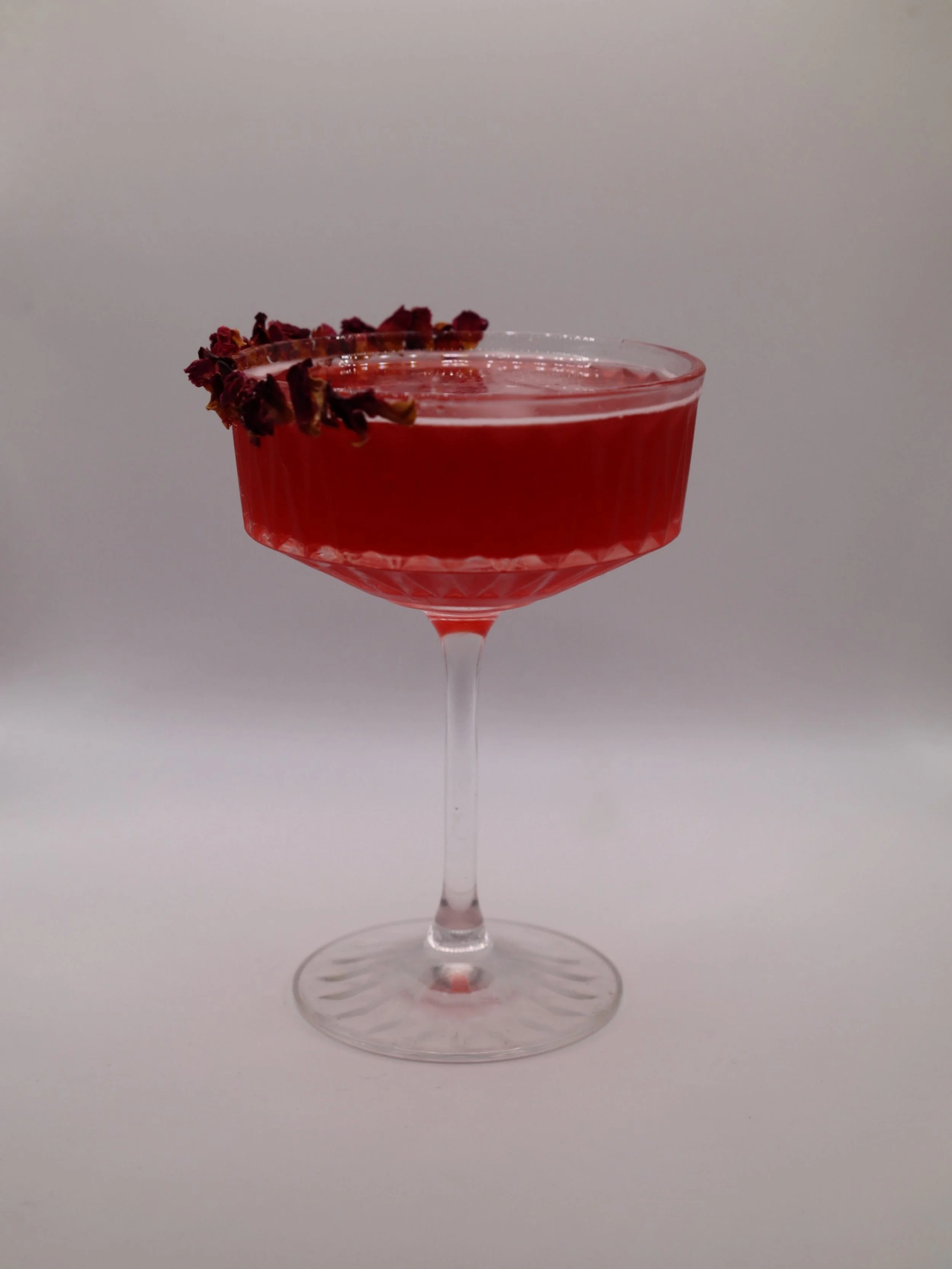 Deep red cocktail in a coupe glass finished with dried floral garnish.
