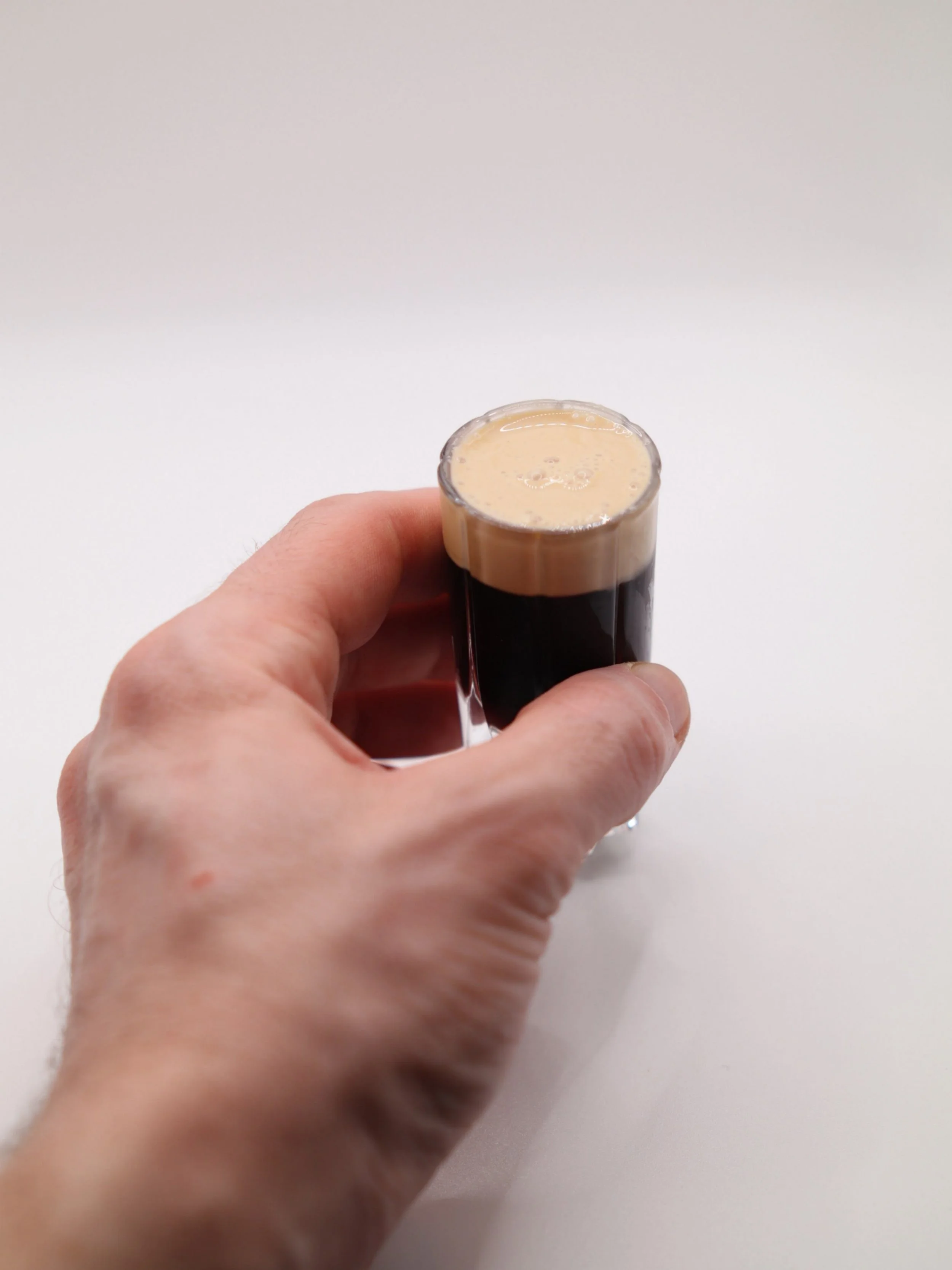 Small dark coffee cocktail shot with a creamy foam top.

