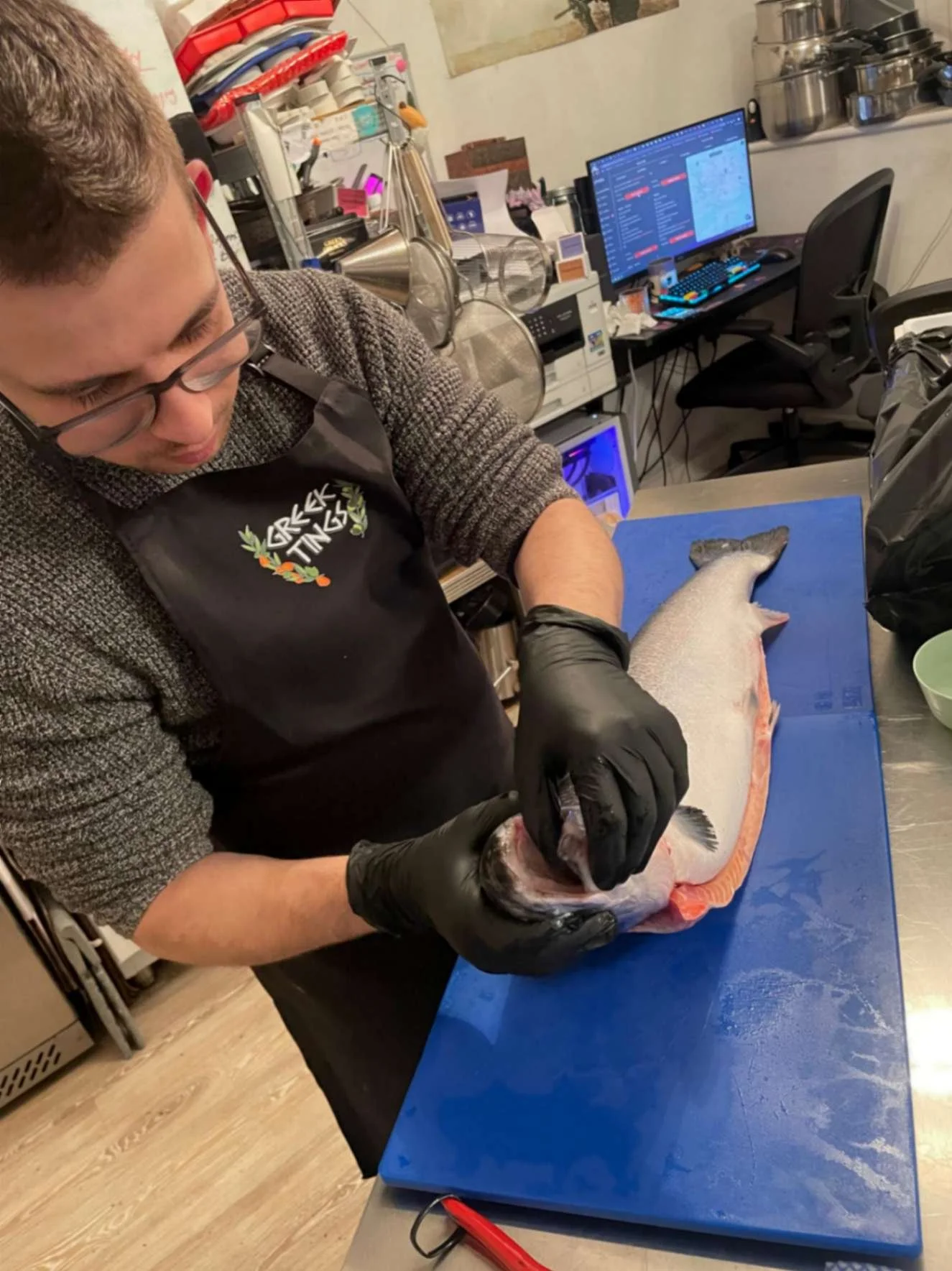 Greek Tings chef preparing a whole fish on a blue board in the kitchen.
