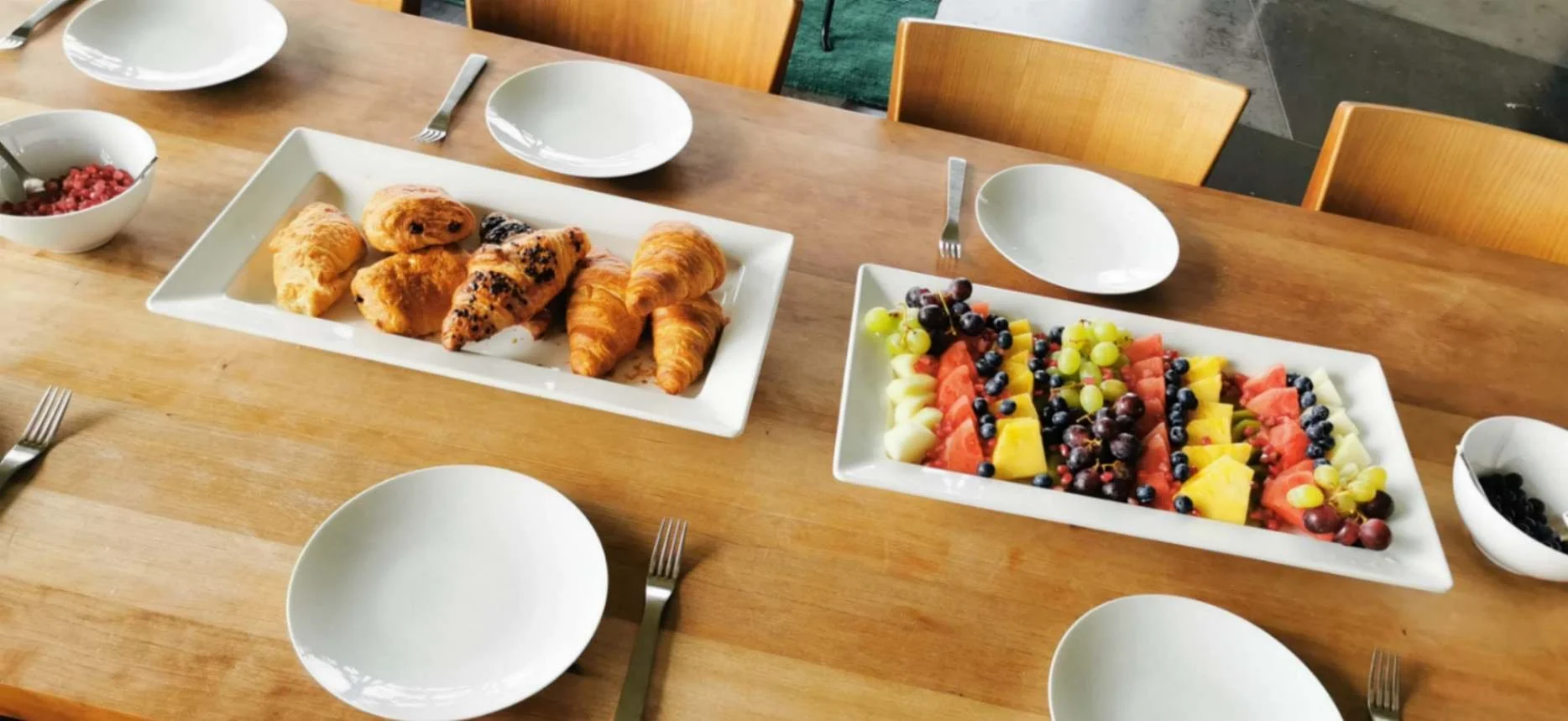 Breakfast table set with pastries, croissants and a colourful fresh fruit platter.
