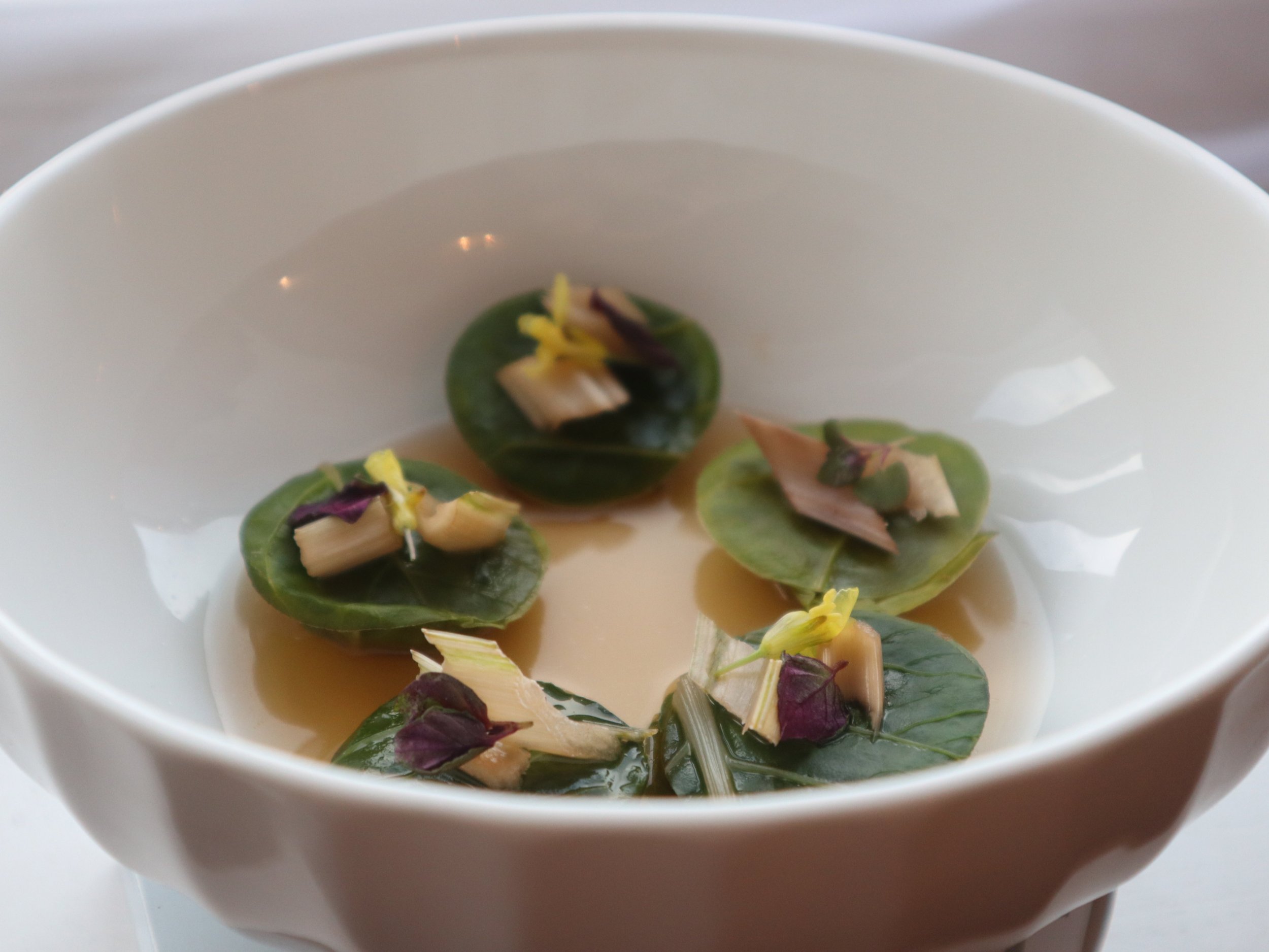 Delicate leaf-wrapped raviolli served in a clear broth with fine herb garnish