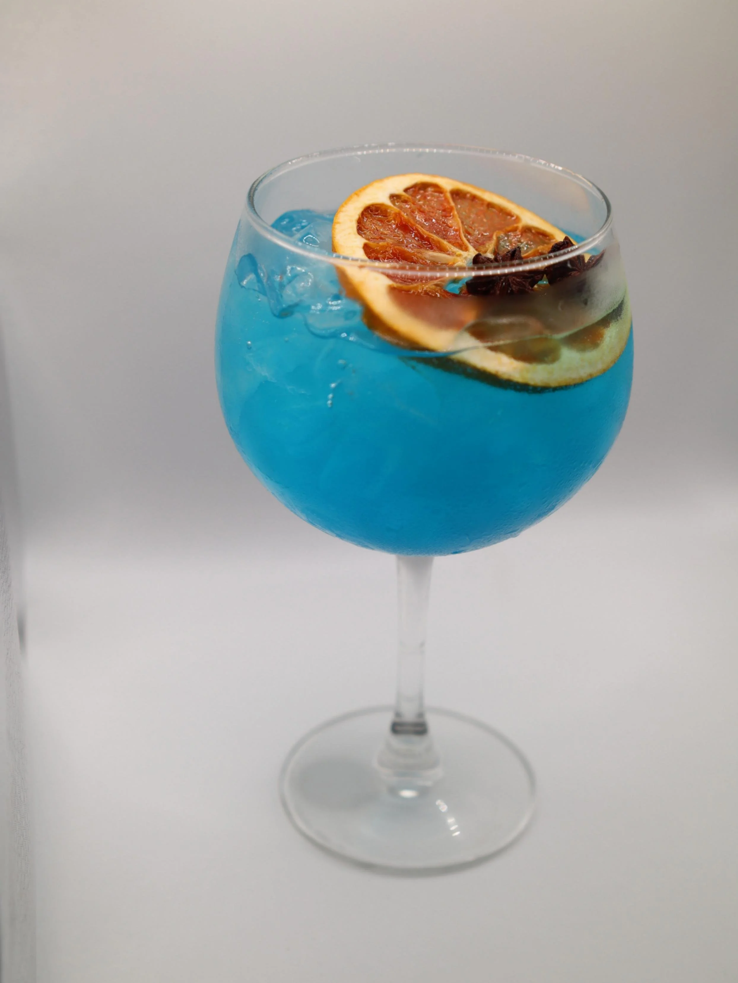 Bright blue cocktail in a goblet with dried citrus and star anise garnish.
