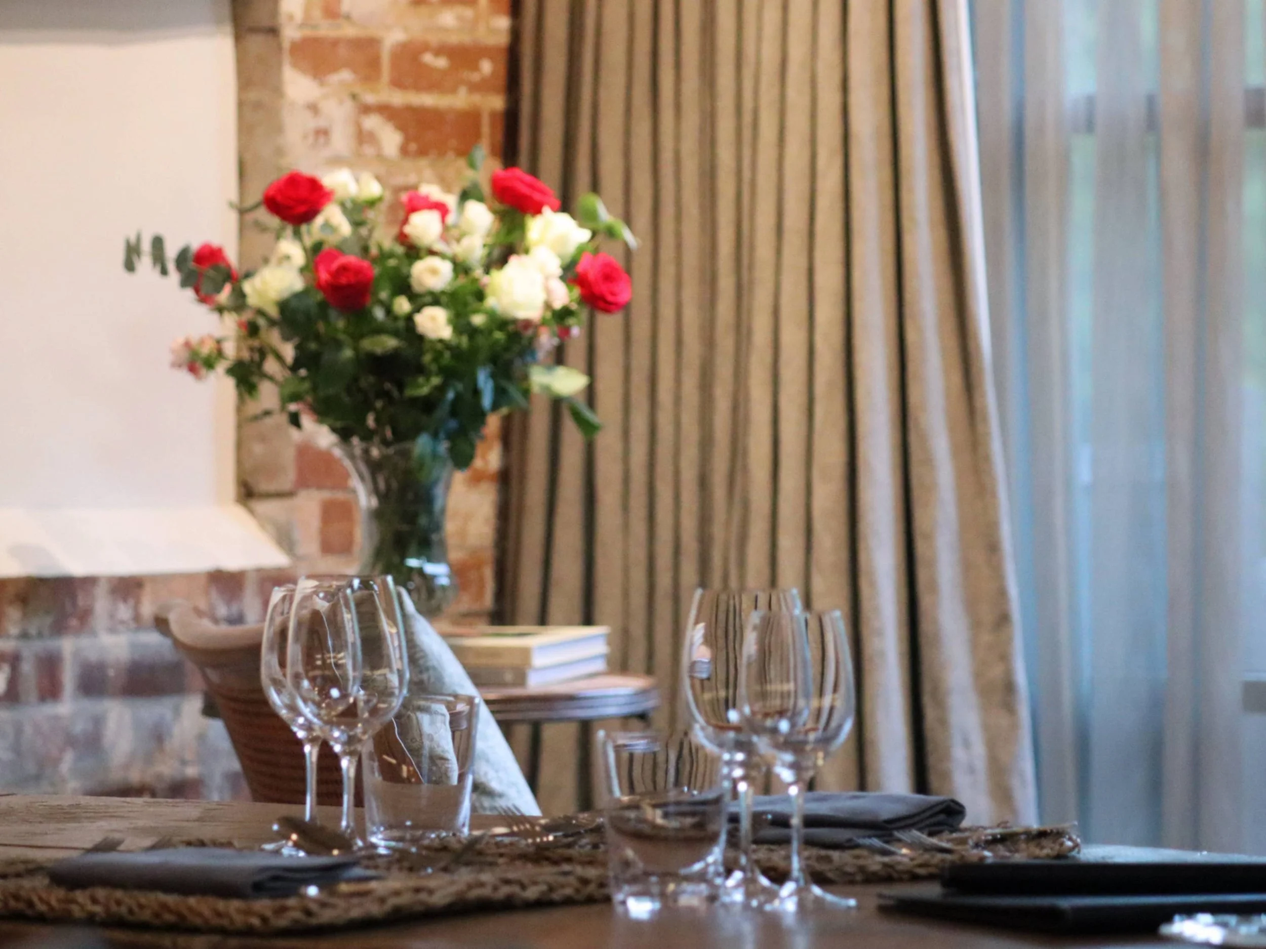 Private dining table set with wine glasses, neutral linen and a red-and-white floral arrangement.