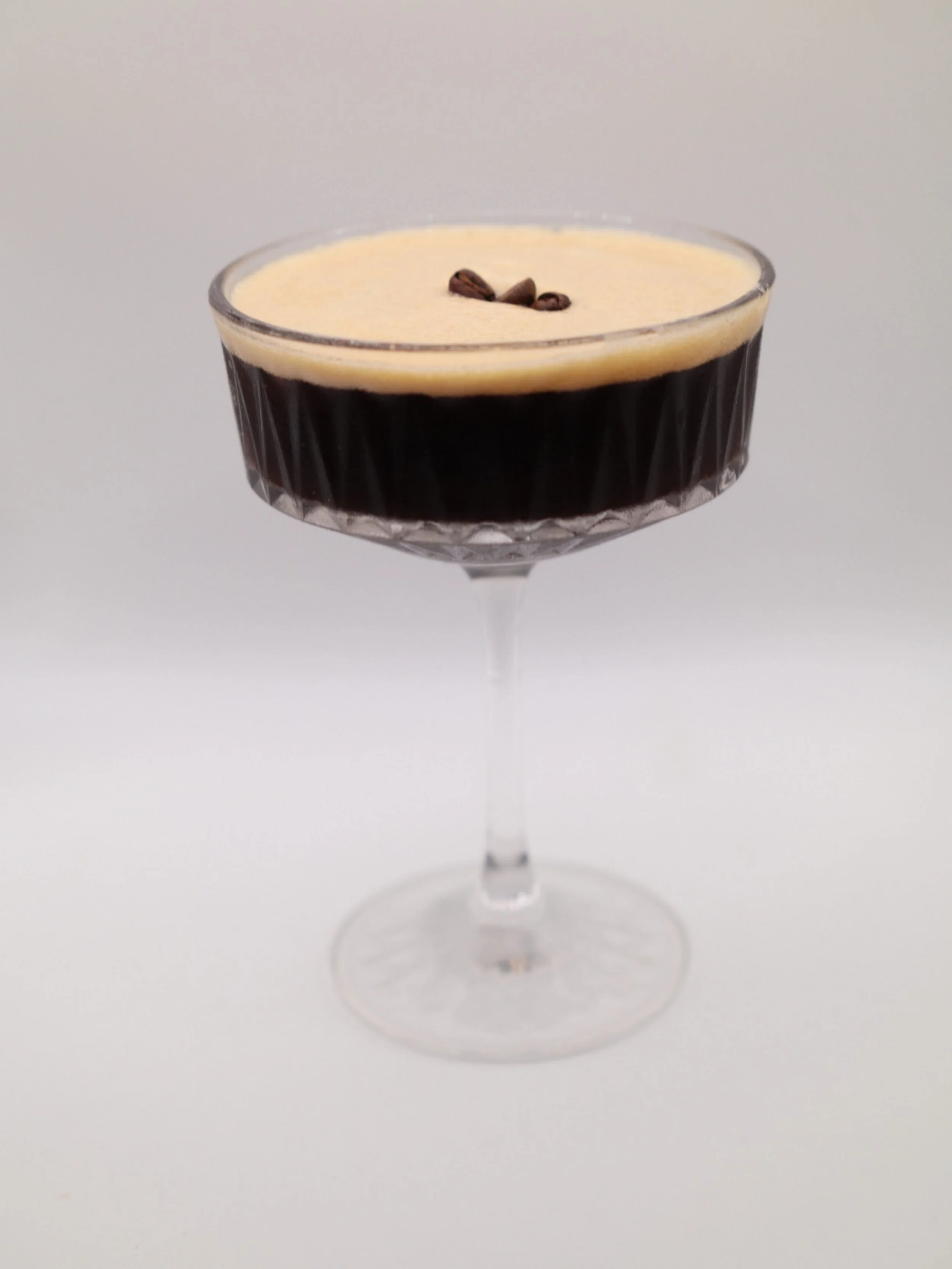 Espresso martini-style cocktail with a creamy foam top and coffee bean garnish.
