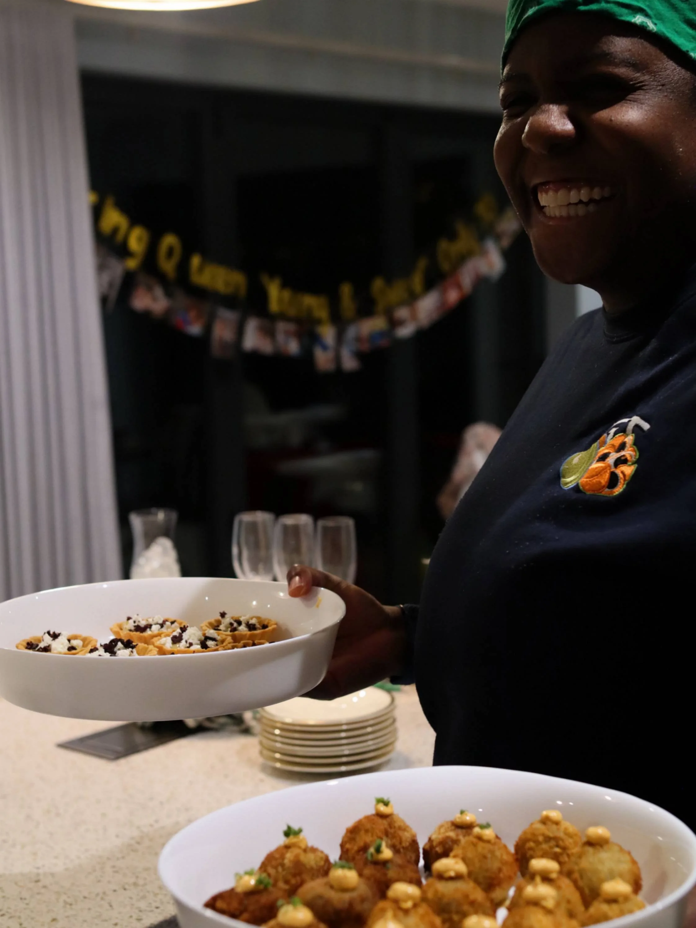 Greek Tings chef smiling with bowls of tartlets and golden croquettes before service.
