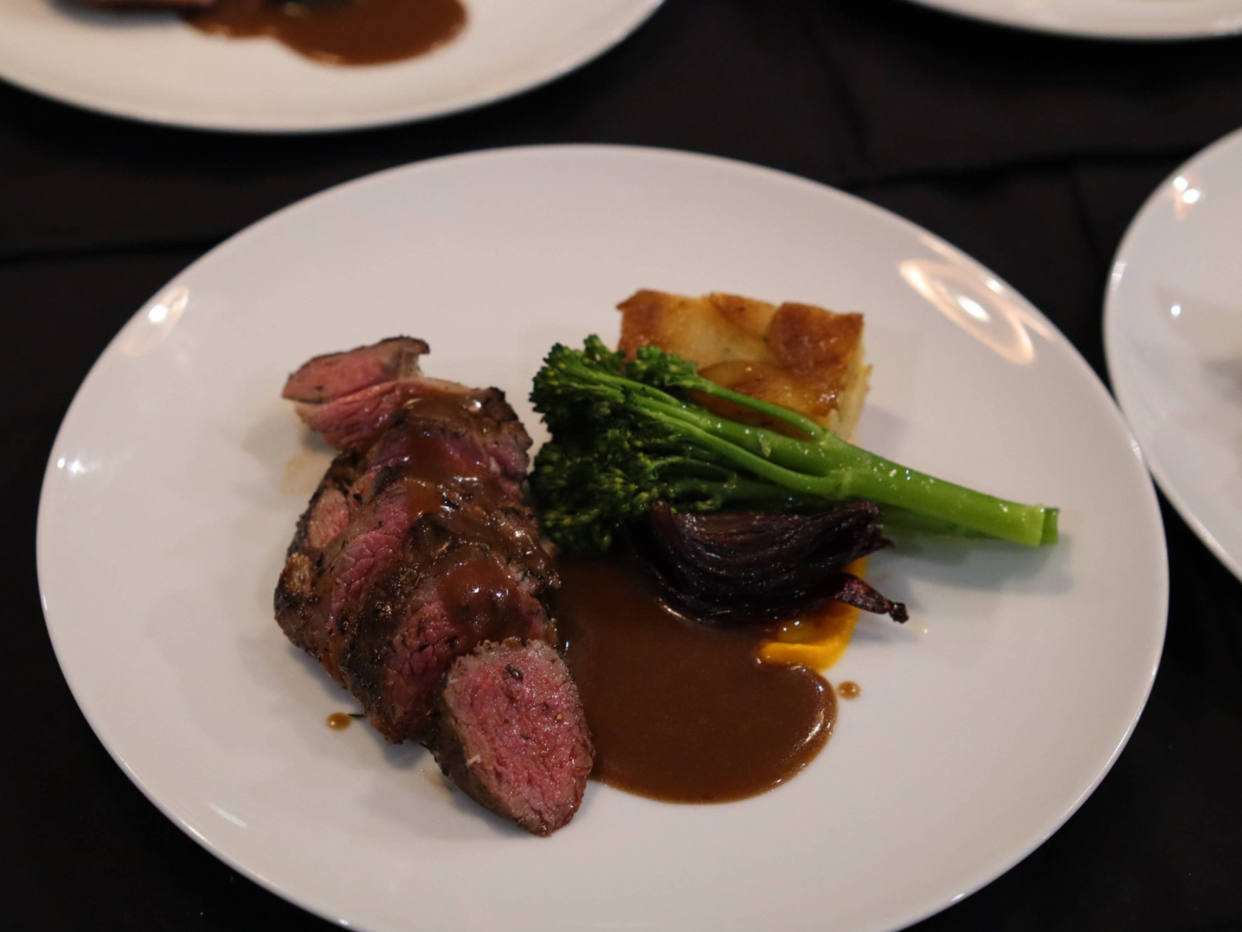  Sliced roast meat with jus, broccolini, roasted onion and layered potato terrine.