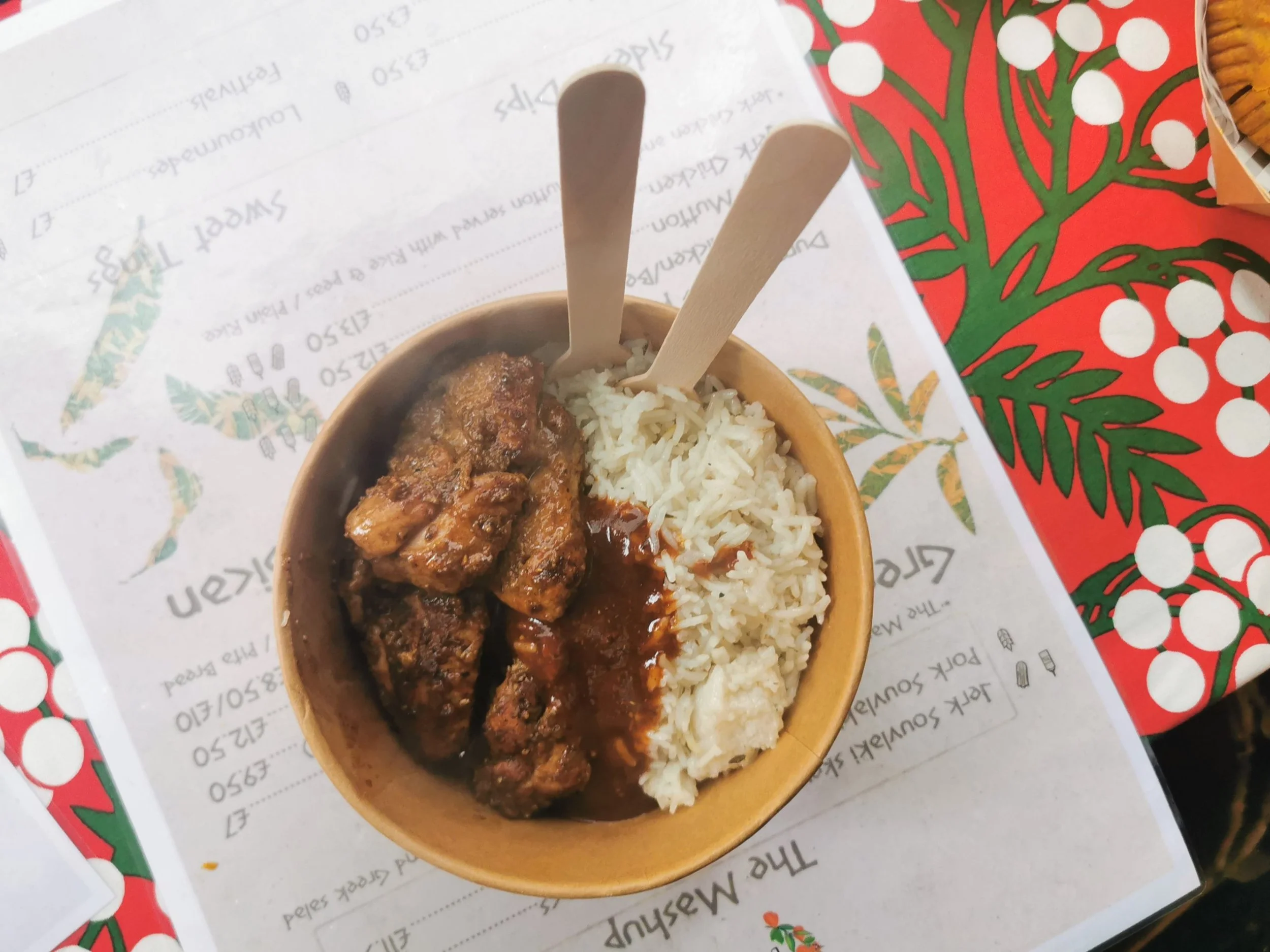 1. Jerk chicken served with rice and sauce in a takeaway bowl at a Greek Tings Jamaican food event.