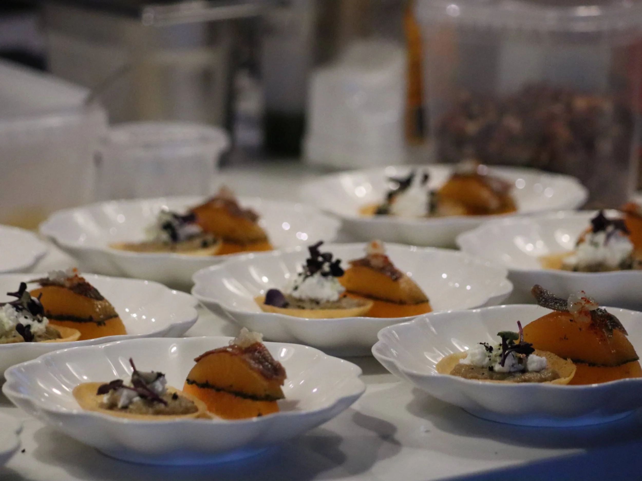 Rows of elegant fine dining canapés with orange purée, crisp base and delicate garnish.
