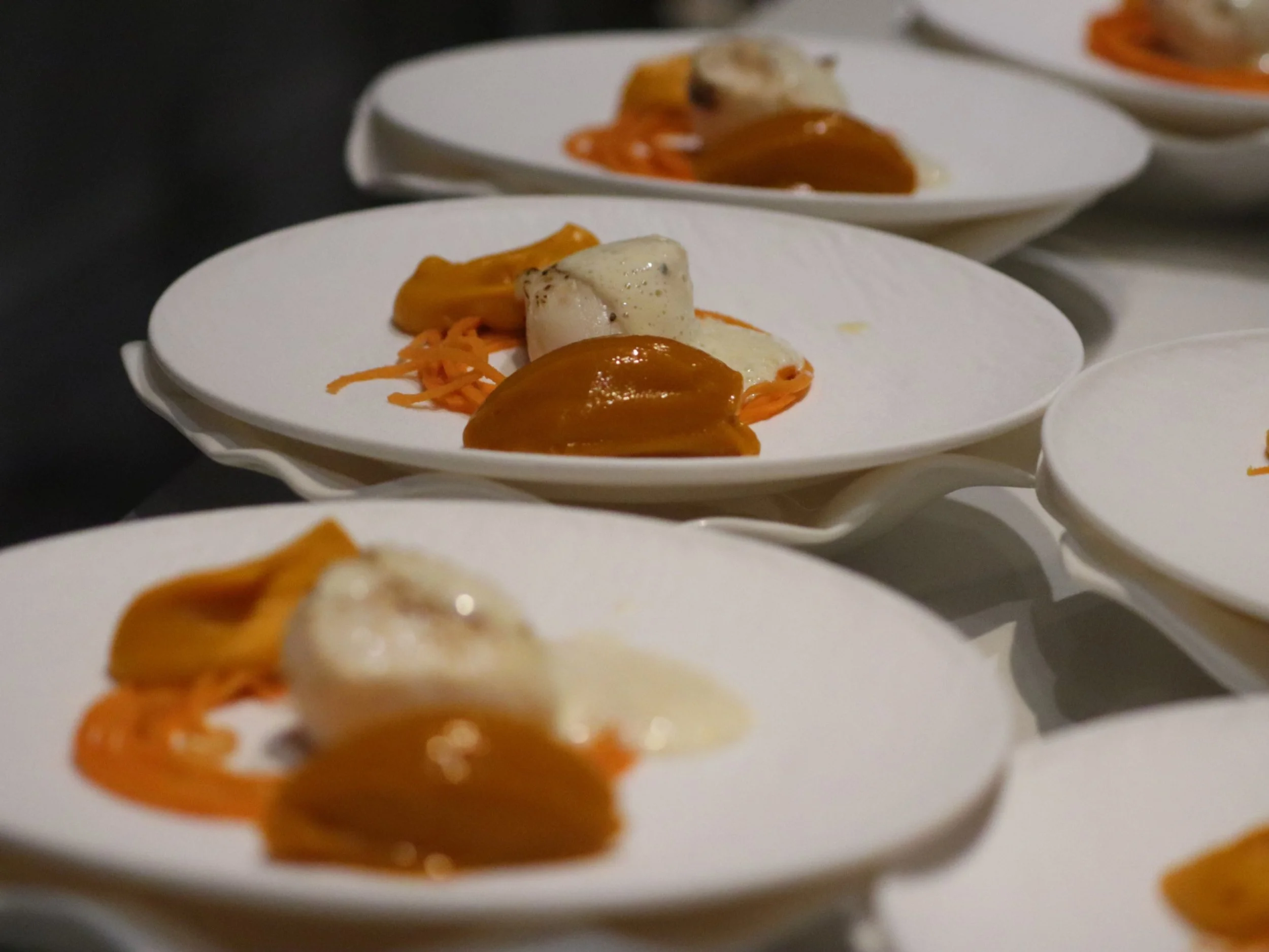  Rows of plated seared scallop courses with orange purée ready for private dining service.