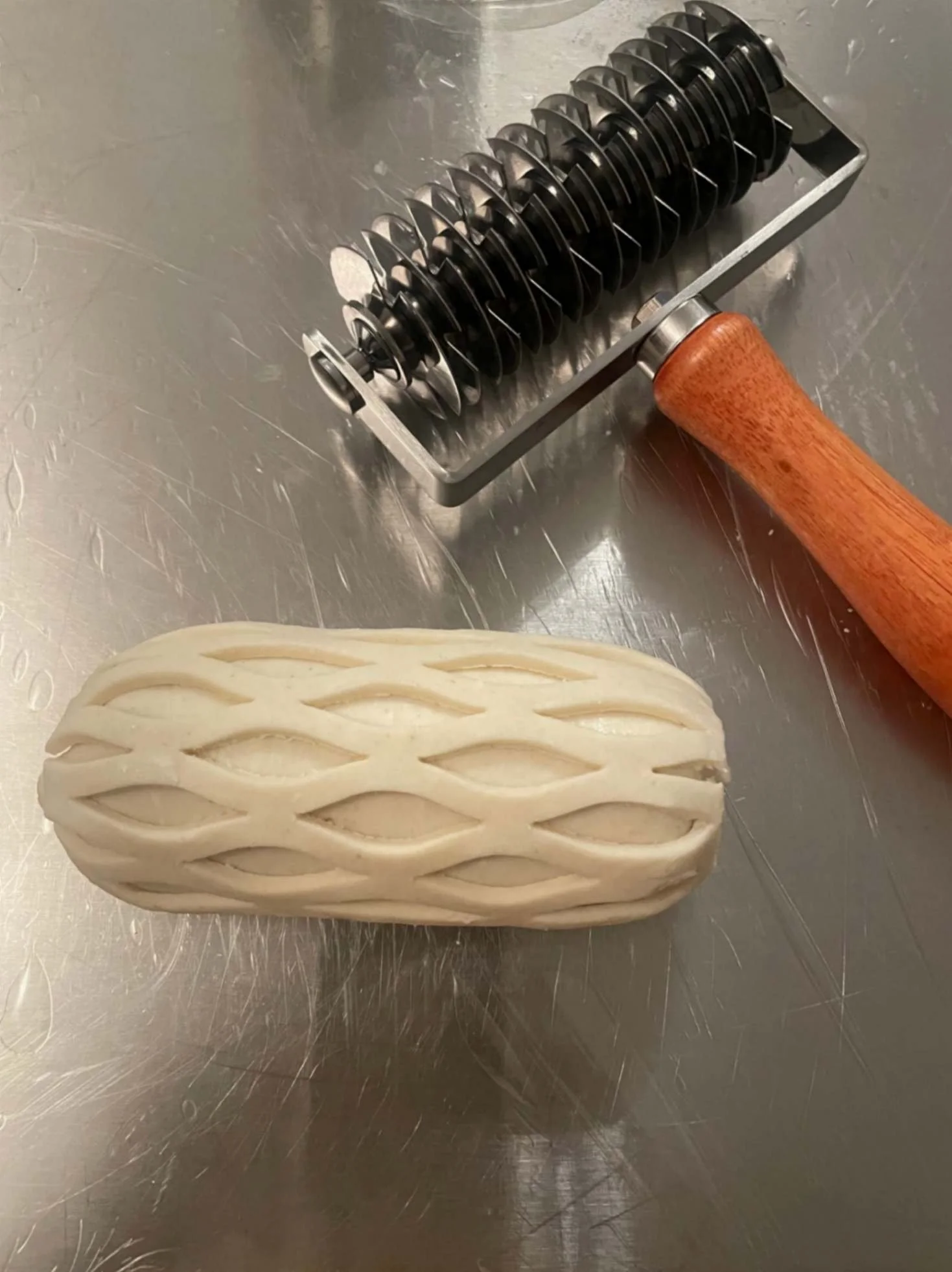 Pastry lattice cutter beside a wrapped pastry roll during kitchen preparation