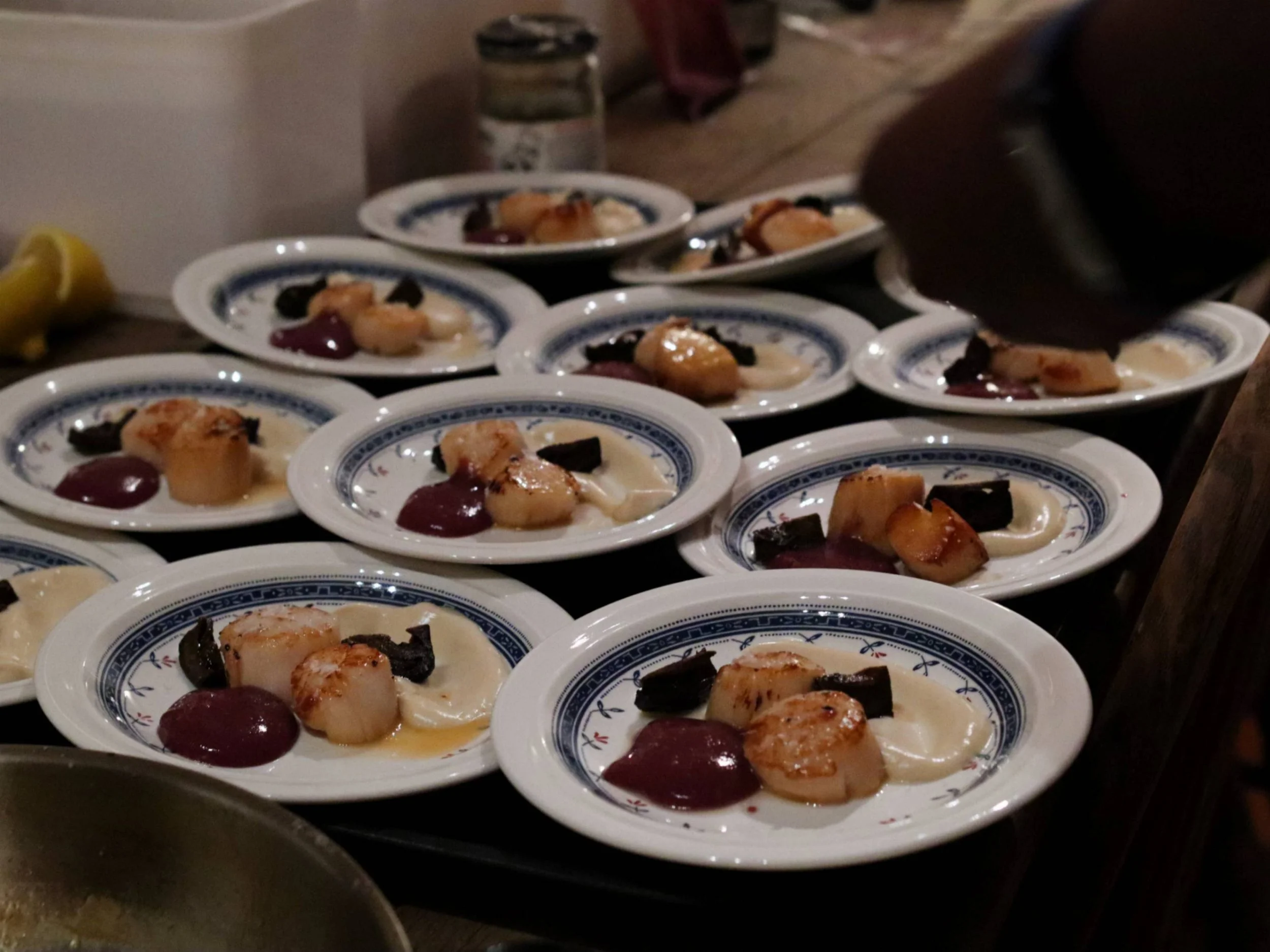Rows of seared scallop starters with colourful purées and fine garnish.
