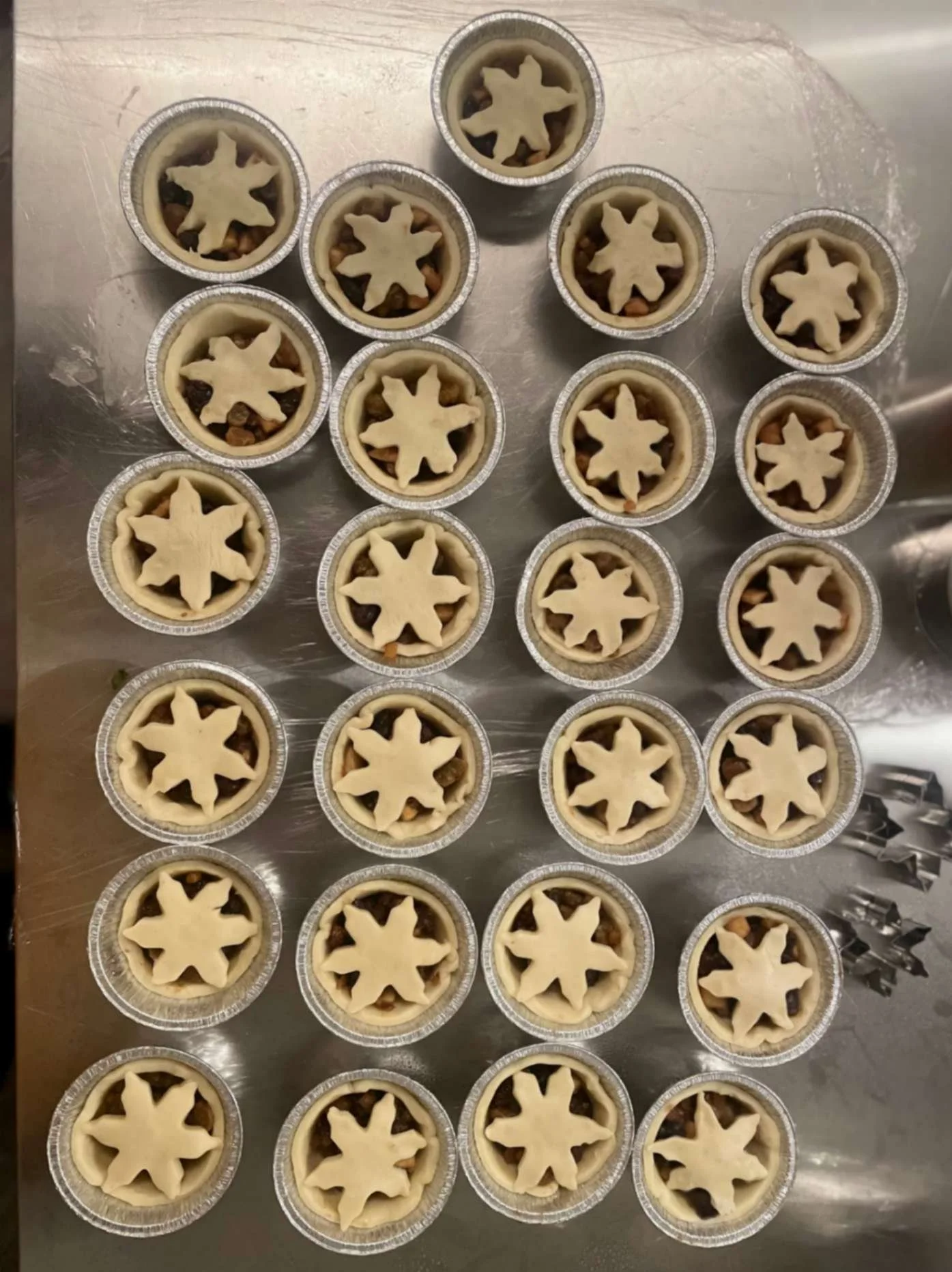 Rows of handmade unbaked mince pies topped with pastry stars.

