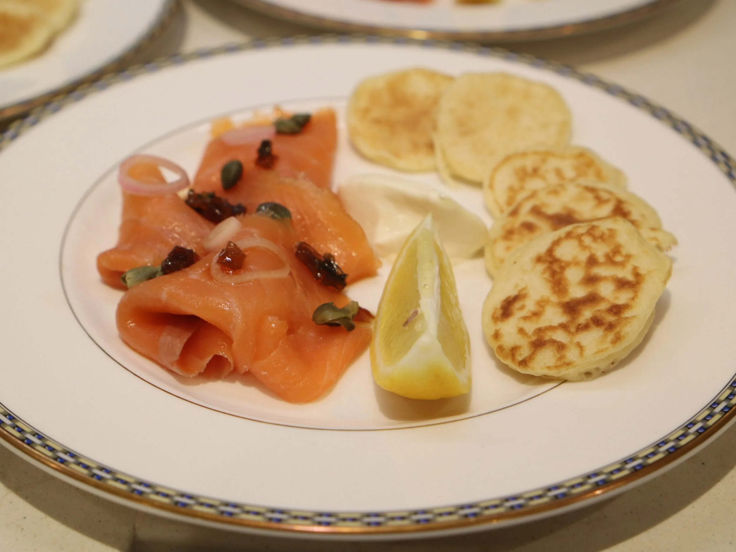 Smoked salmon with mini blinis, lemon and capers on a plated British starter.
