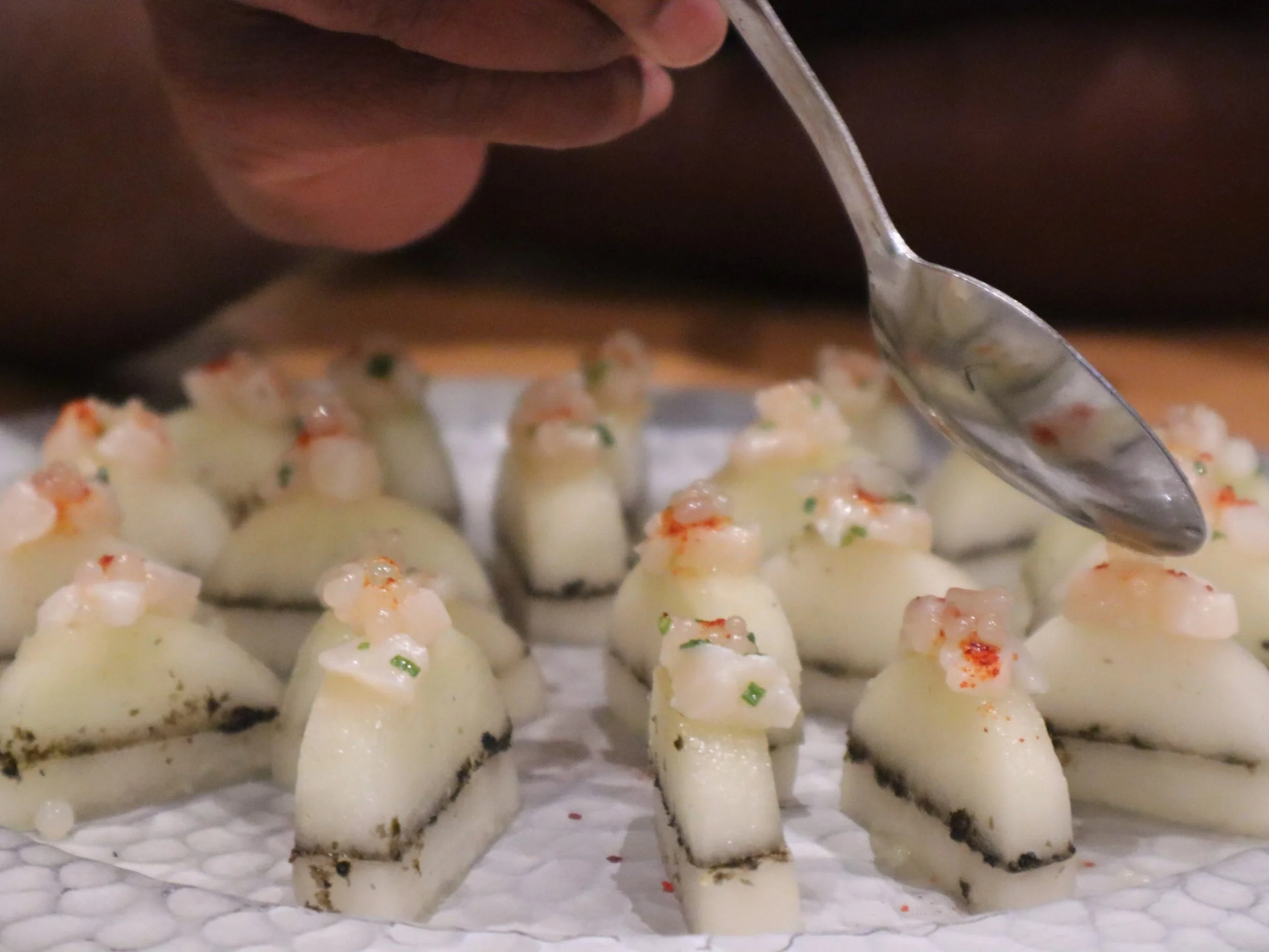 Delicate layered canapés topped with finely diced garnish during private chef preparation.
