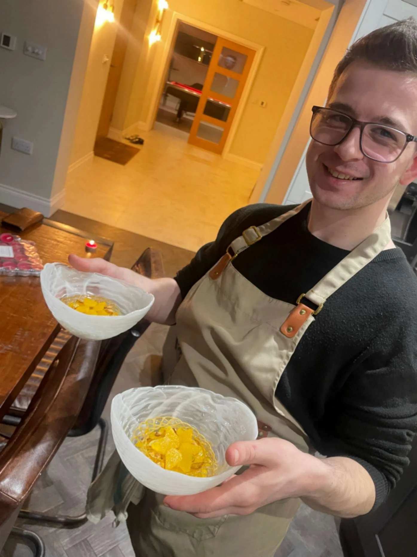  Greek Tings chef holding two orange plated dessert courses during private dining service.
