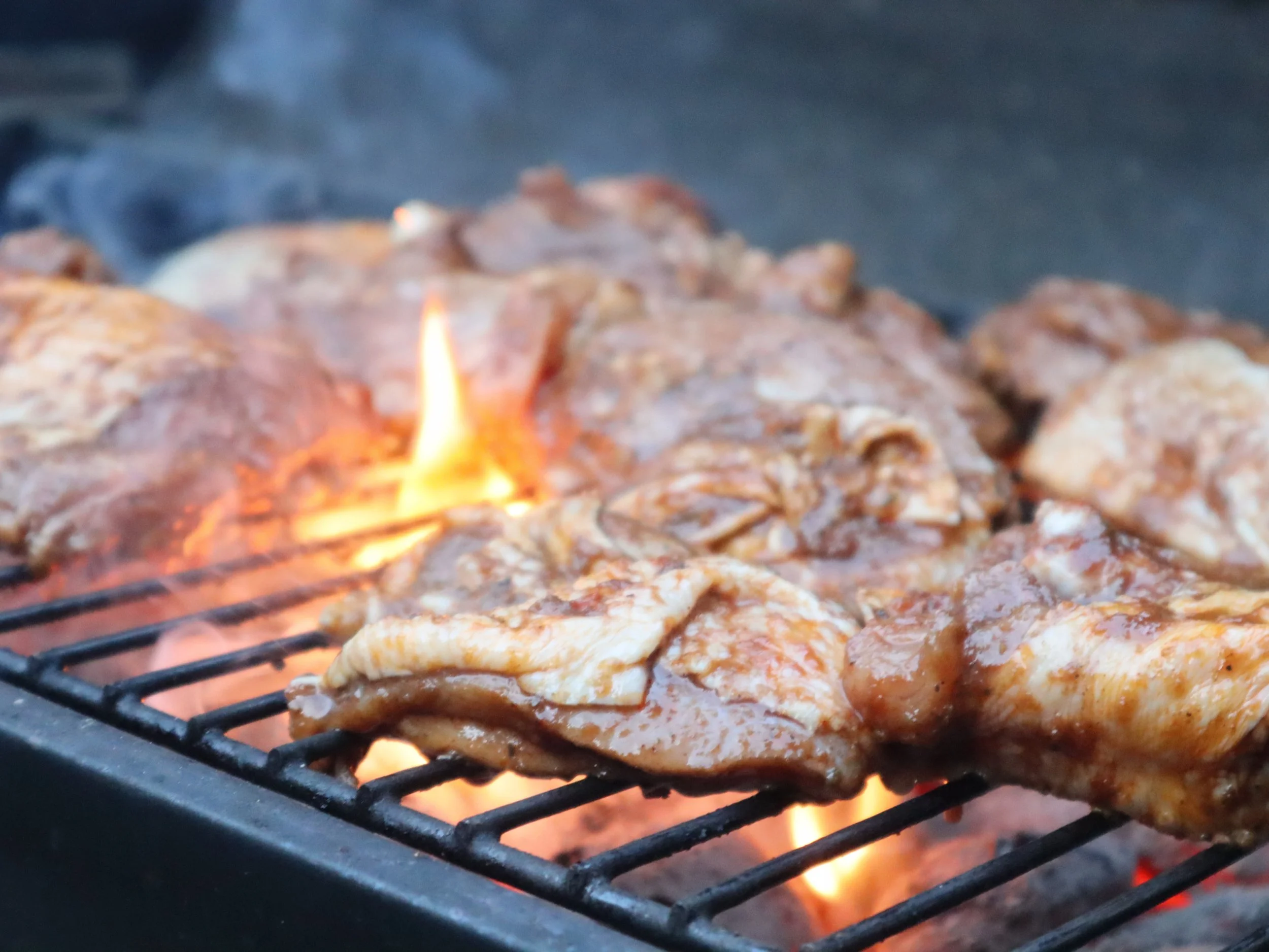 Marinated jerk chicken grilling over open flames for a Greek Tings barbecue event.
