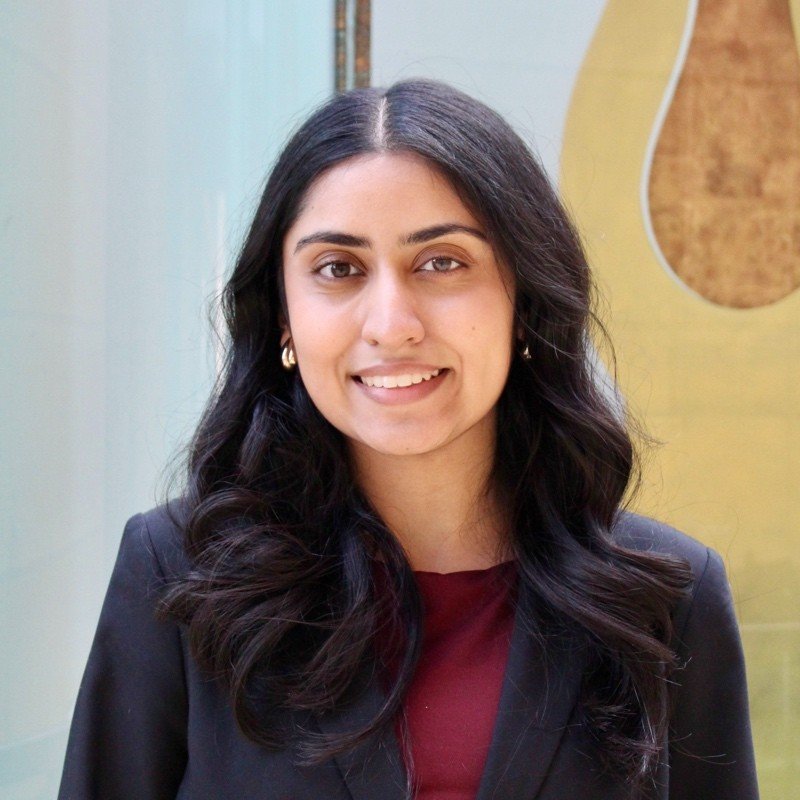 A woman with long dark hair, wearing a black blazer and a maroon top, smiling and looking at the camera.