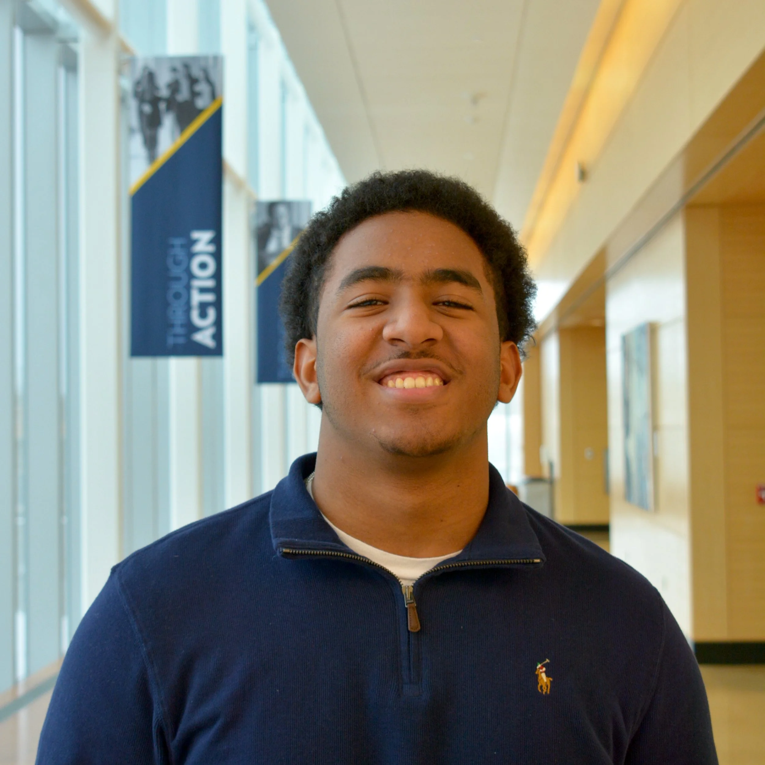 Young man smiling in a hallway with banners that say "Thought Action" in the background.