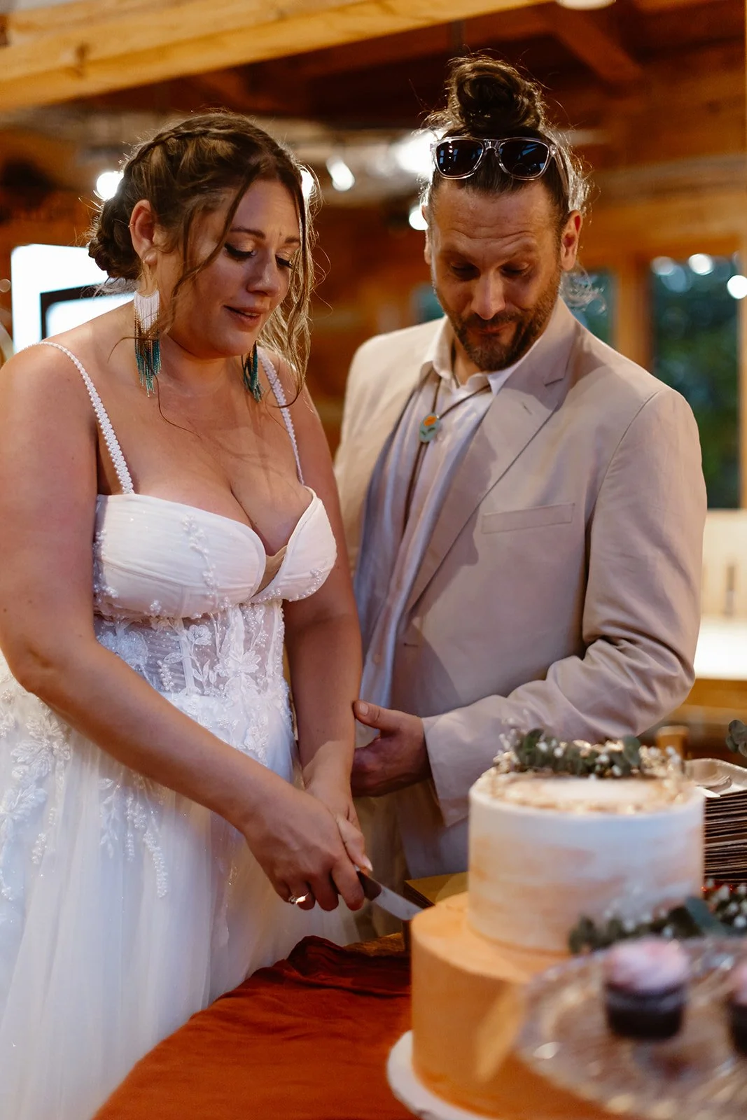 A bride and groom cutting their wedding cake in a rustic indoor setting.